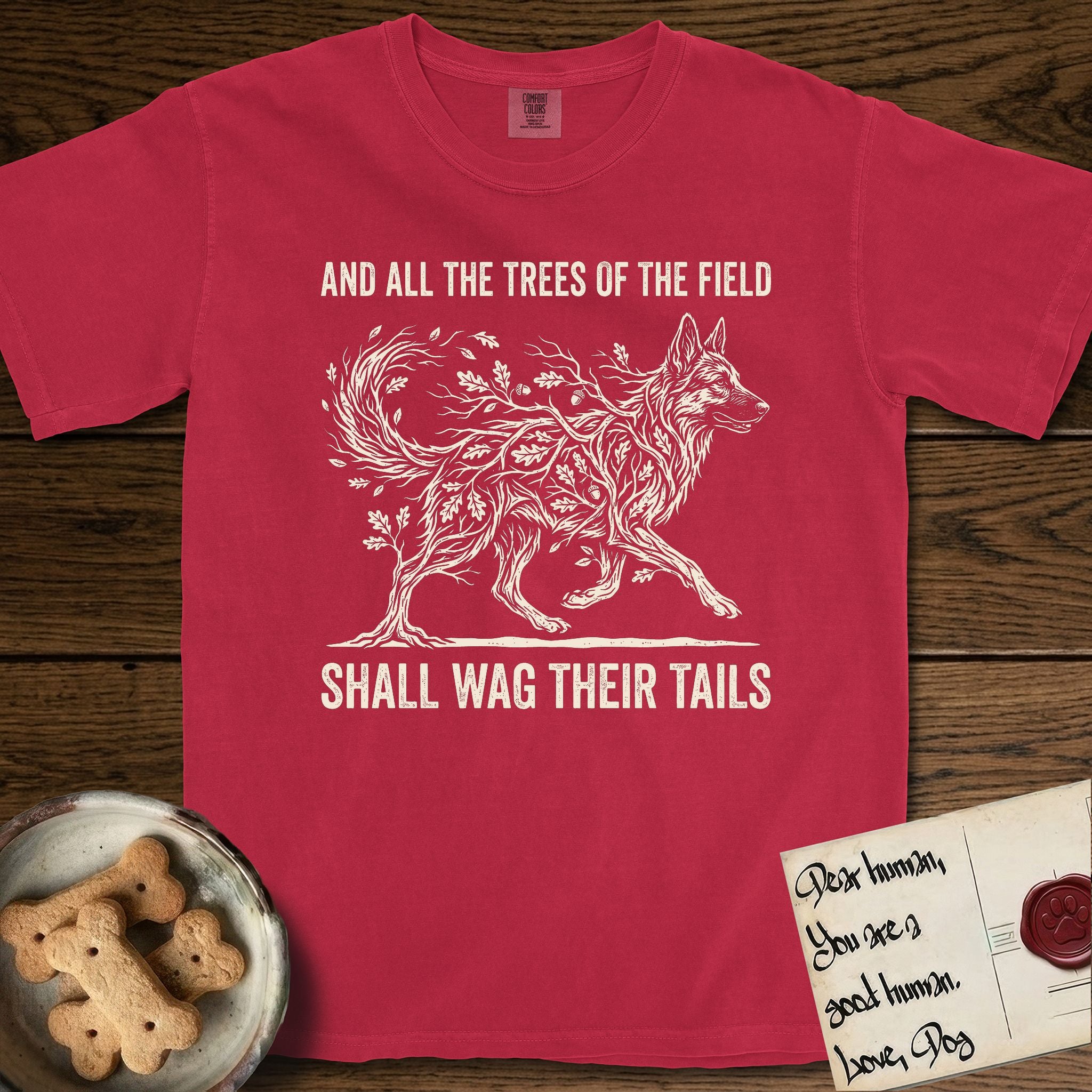 Trees of the Field German Shepherd T-Shirt flat lay in Red, featuring a vintage woodcut illustration of a German Shepherd formed of oak branches with acorns, mid-stride, with the words And All the Trees of the Field Shall Wag Their Tails.