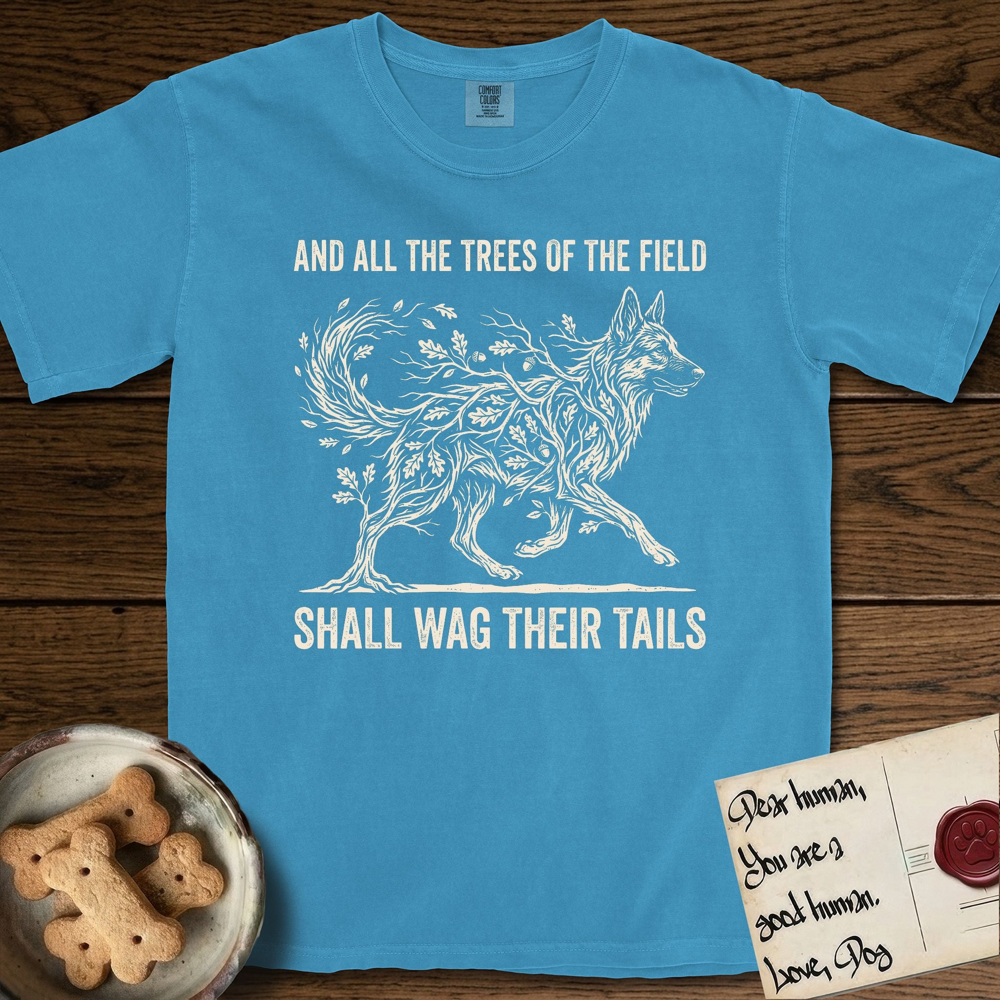 Trees of the Field German Shepherd T-Shirt flat lay in Royal Caribe, featuring a vintage woodcut illustration of a German Shepherd formed of oak branches with acorns, mid-stride, with the words And All the Trees of the Field Shall Wag Their Tails.
