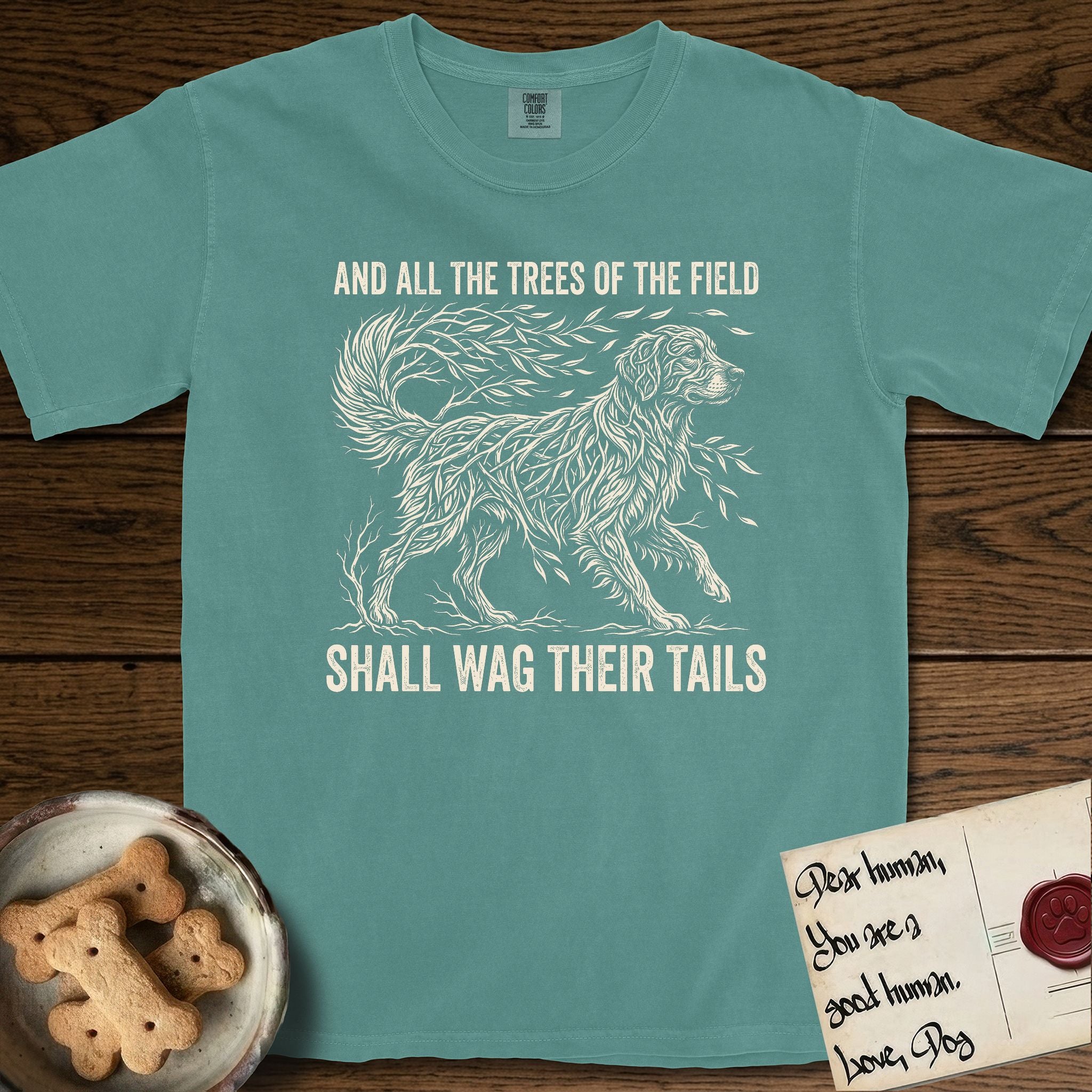 Trees of the Field Golden Retriever T-Shirt flat lay in Blue Spruce, featuring a vintage woodcut illustration of a Golden Retriever formed of flowing willow branches, mid-stride, with the words And All the Trees of the Field Shall Wag Their Tails.