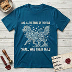 Trees of the Field Goldendoodle T-Shirt flat lay in Antique Sapphire, featuring a vintage woodcut illustration of a Goldendoodle formed of ginkgo branches with fan-shaped leaves, mid-stride, with the words And All the Trees of the Field Shall Wag Their Tails.