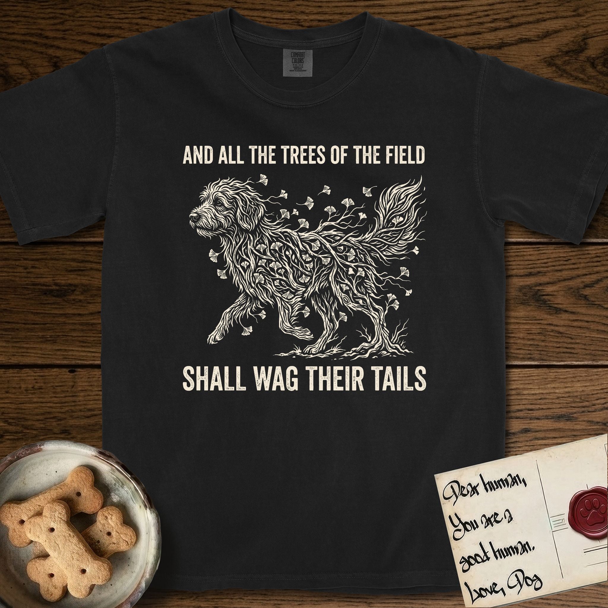 Trees of the Field Goldendoodle T-Shirt flat lay in Black, featuring a vintage woodcut illustration of a Goldendoodle formed of ginkgo branches with fan-shaped leaves, mid-stride, with the words And All the Trees of the Field Shall Wag Their Tails.