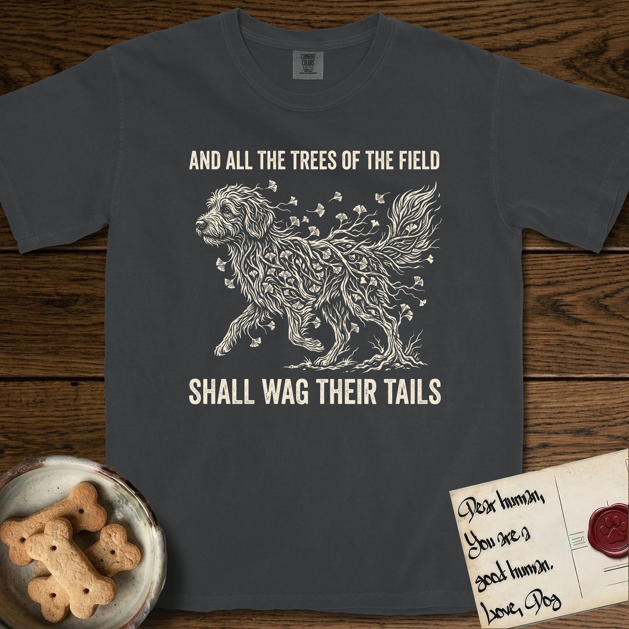 Trees of the Field Goldendoodle T-Shirt flat lay in Graphite, featuring a vintage woodcut illustration of a Goldendoodle formed of ginkgo branches with fan-shaped leaves, mid-stride, with the words And All the Trees of the Field Shall Wag Their Tails.