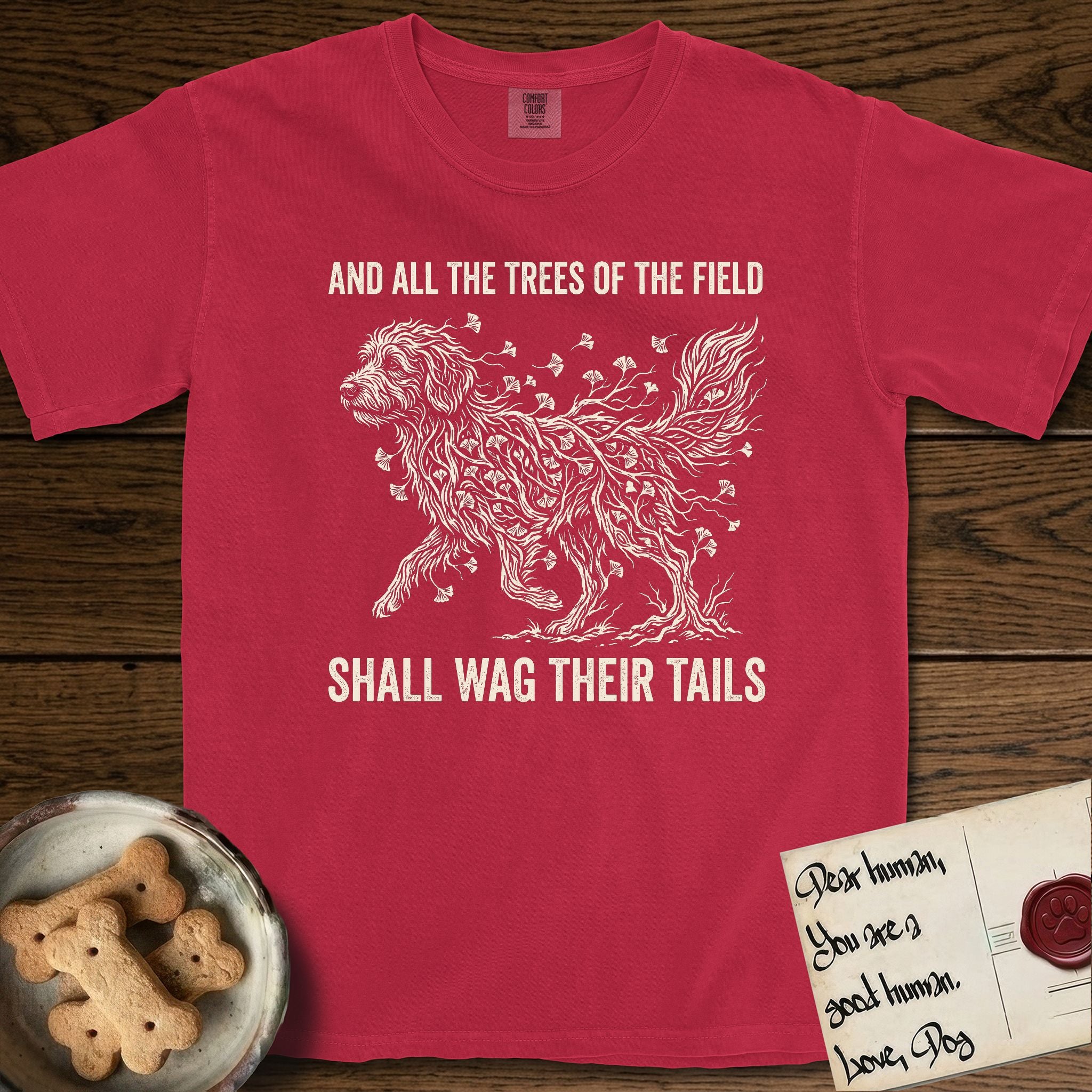 Trees of the Field Goldendoodle T-Shirt flat lay in Red, featuring a vintage woodcut illustration of a Goldendoodle formed of ginkgo branches with fan-shaped leaves, mid-stride, with the words And All the Trees of the Field Shall Wag Their Tails.