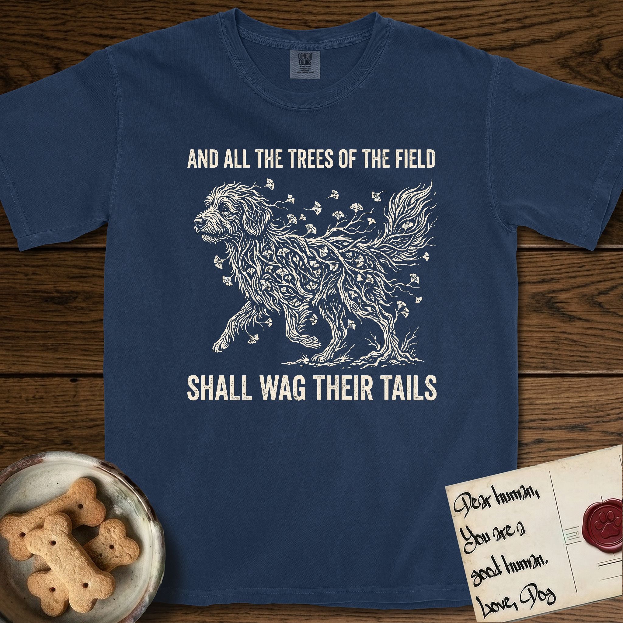 Trees of the Field Goldendoodle T-Shirt flat lay in True Navy, featuring a vintage woodcut illustration of a Goldendoodle formed of ginkgo branches with fan-shaped leaves, mid-stride, with the words And All the Trees of the Field Shall Wag Their Tails.