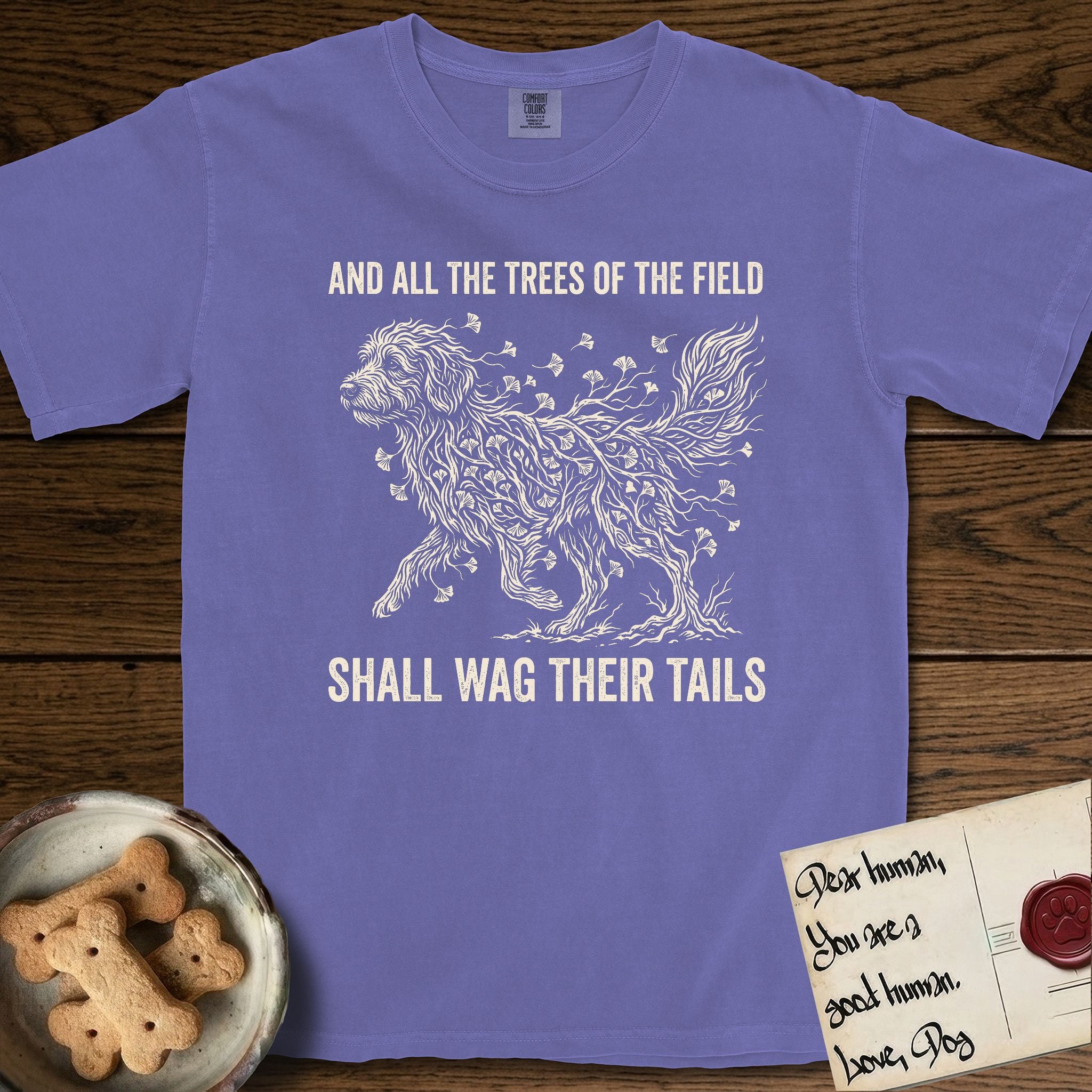 Trees of the Field Goldendoodle T-Shirt flat lay in Violet, featuring a vintage woodcut illustration of a Goldendoodle formed of ginkgo branches with fan-shaped leaves, mid-stride, with the words And All the Trees of the Field Shall Wag Their Tails.