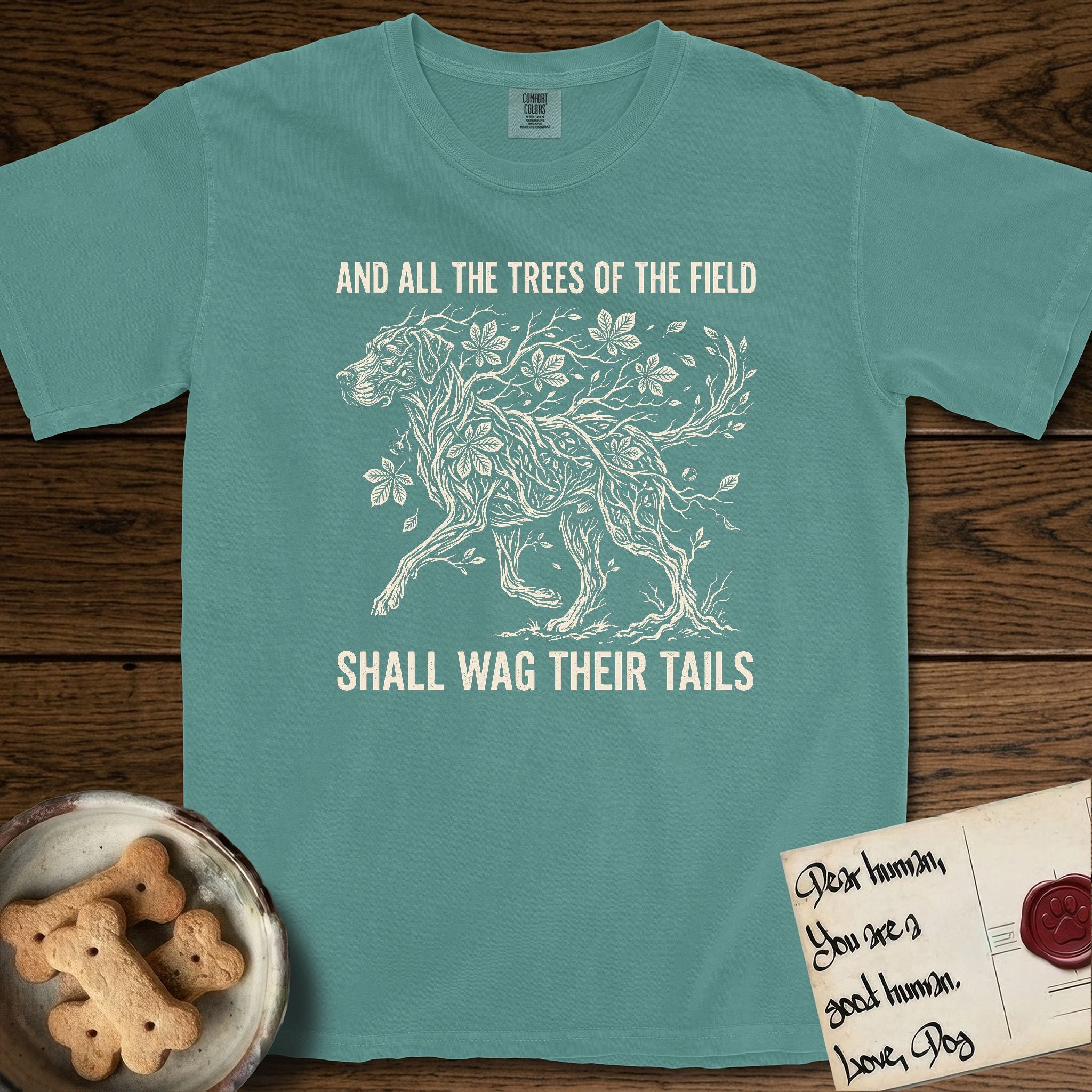 Trees of the Field Great Dane T-Shirt flat lay in Blue Spruce, featuring a vintage woodcut illustration of a Great Dane formed of horse chestnut branches and leaves, mid-stride, with the words And All the Trees of the Field Shall Wag Their Tails.