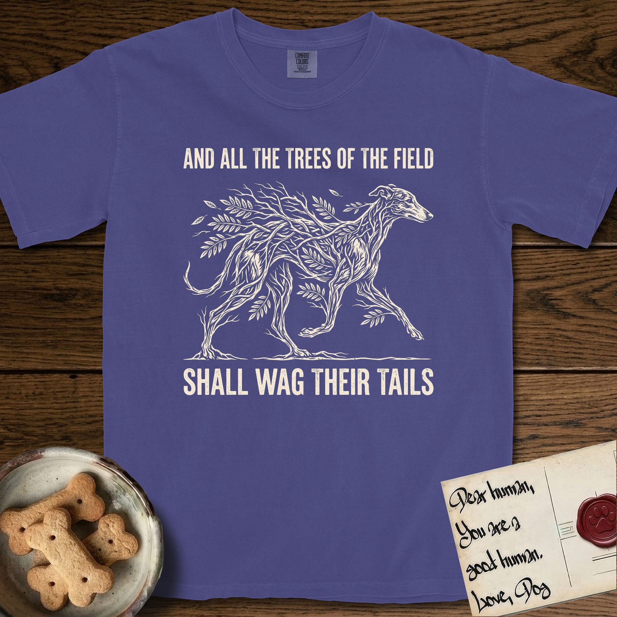 Trees of the Field Greyhound T-Shirt flat lay in Grape, featuring a vintage woodcut illustration of a Greyhound formed of ash branches with streaming leaves, mid-stride, with the words And All the Trees of the Field Shall Wag Their Tails.
