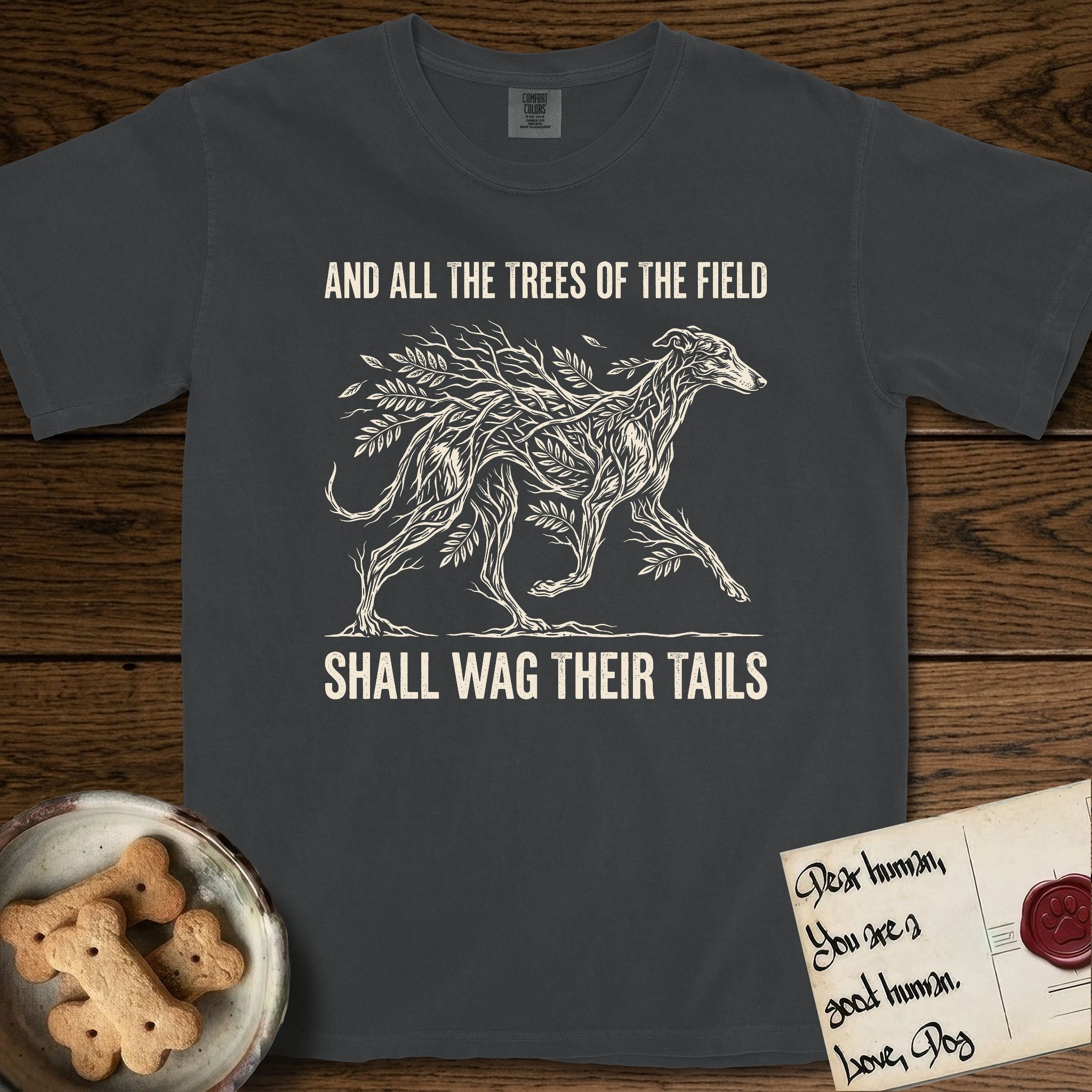 Trees of the Field Greyhound T-Shirt flat lay in Graphite, featuring a vintage woodcut illustration of a Greyhound formed of ash branches with streaming leaves, mid-stride, with the words And All the Trees of the Field Shall Wag Their Tails.