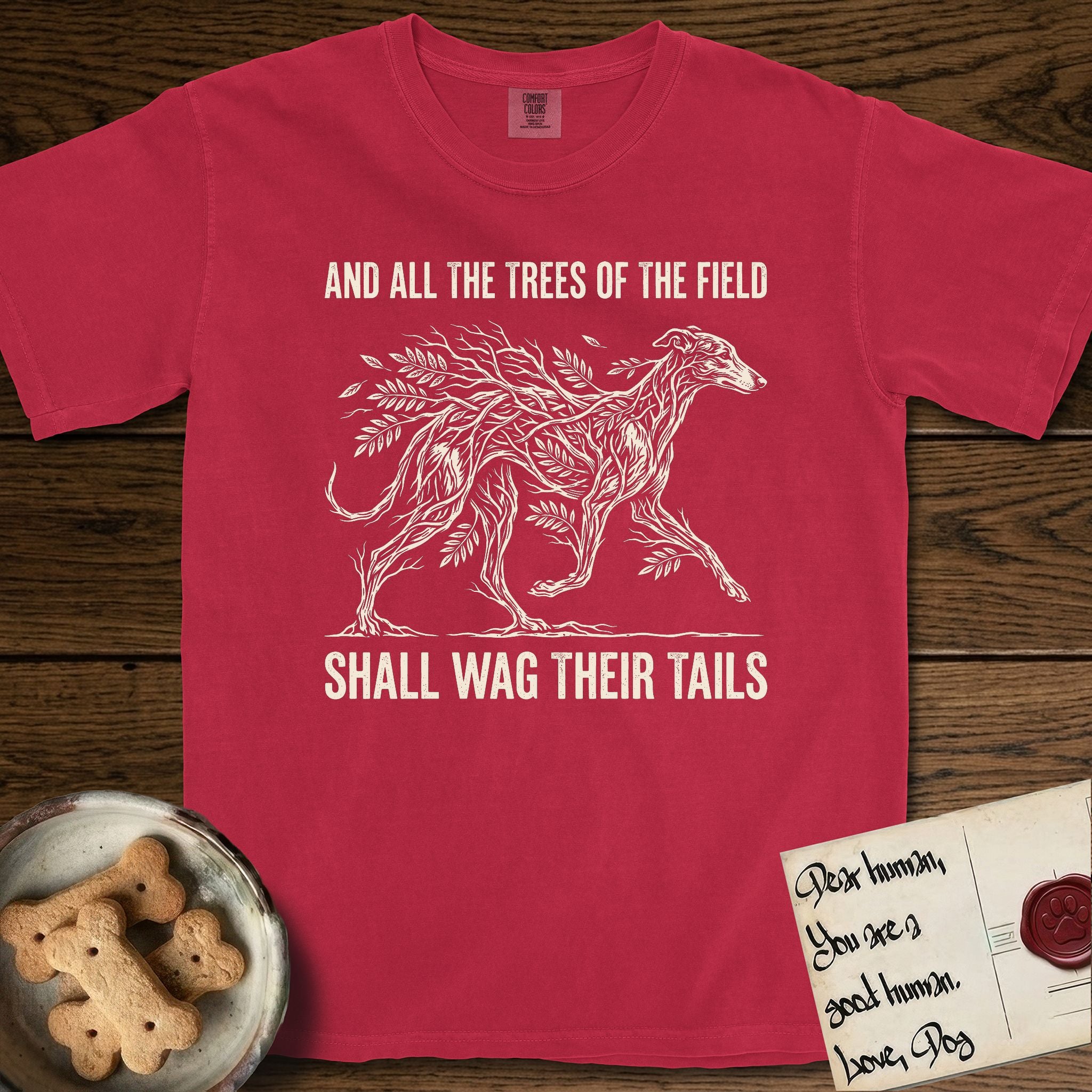Trees of the Field Greyhound T-Shirt flat lay in Red, featuring a vintage woodcut illustration of a Greyhound formed of ash branches with streaming leaves, mid-stride, with the words And All the Trees of the Field Shall Wag Their Tails.