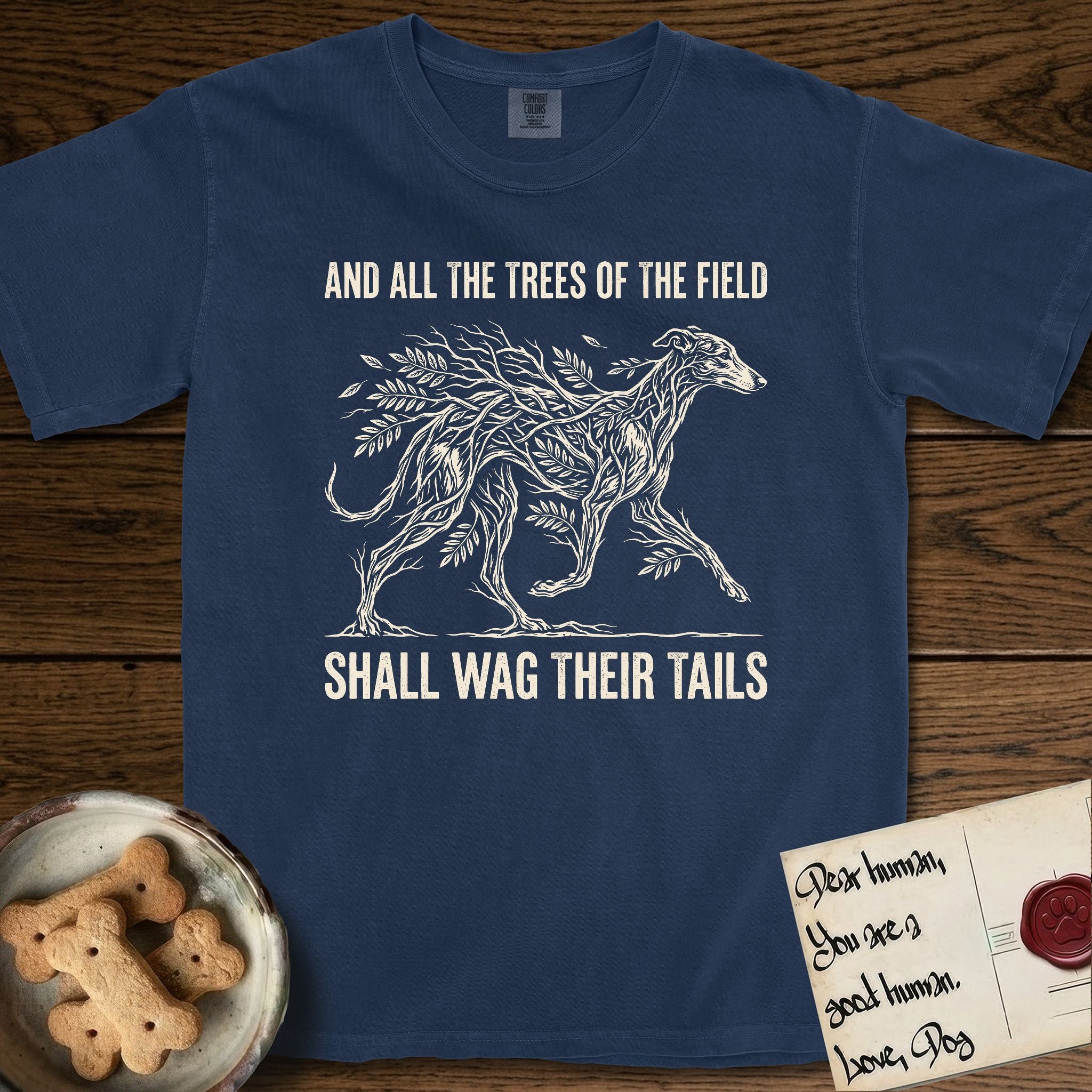 Trees of the Field Greyhound T-Shirt flat lay in True Navy, featuring a vintage woodcut illustration of a Greyhound formed of ash branches with streaming leaves, mid-stride, with the words And All the Trees of the Field Shall Wag Their Tails.