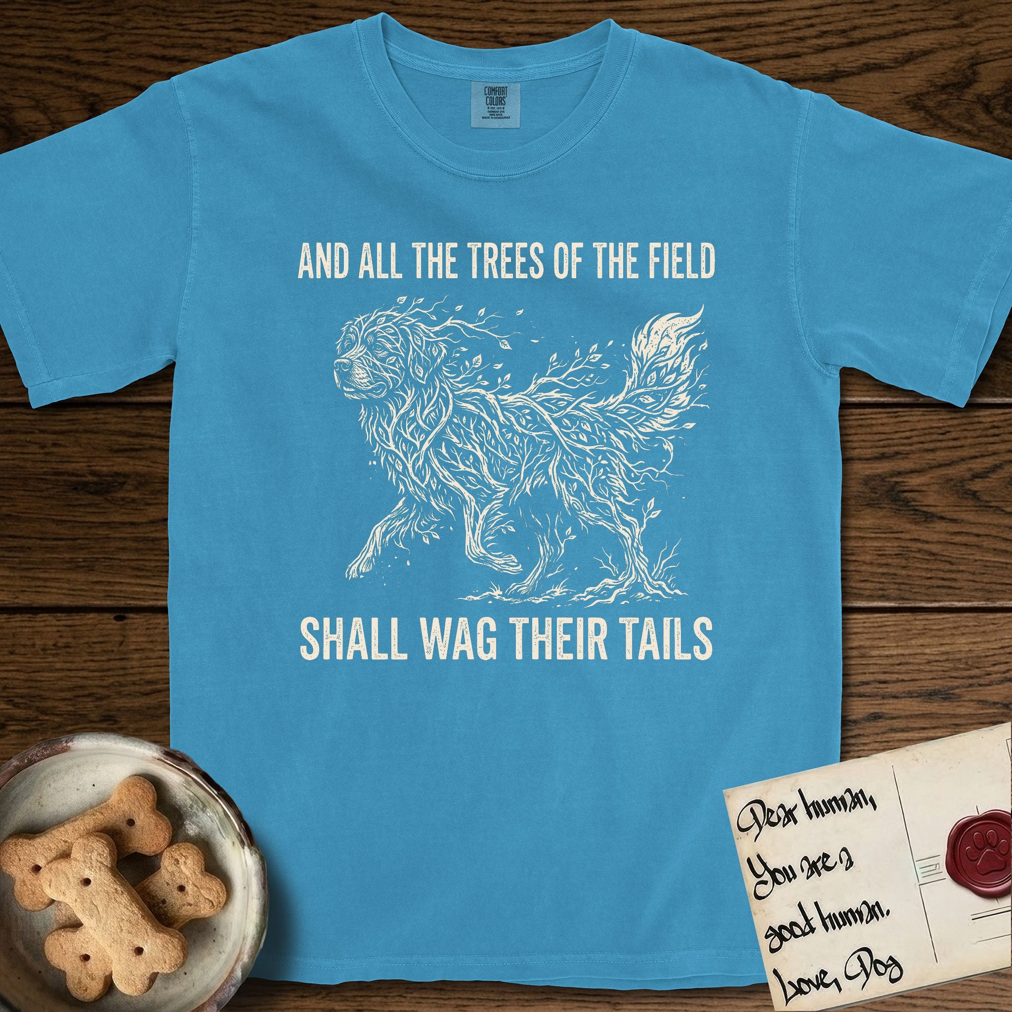 Trees of the Field Newfoundland T-Shirt flat lay in Royal Caribe, featuring a vintage woodcut illustration of a Newfoundland formed of linden branches in full leaf, mid-stride, with the words And All the Trees of the Field Shall Wag Their Tails.