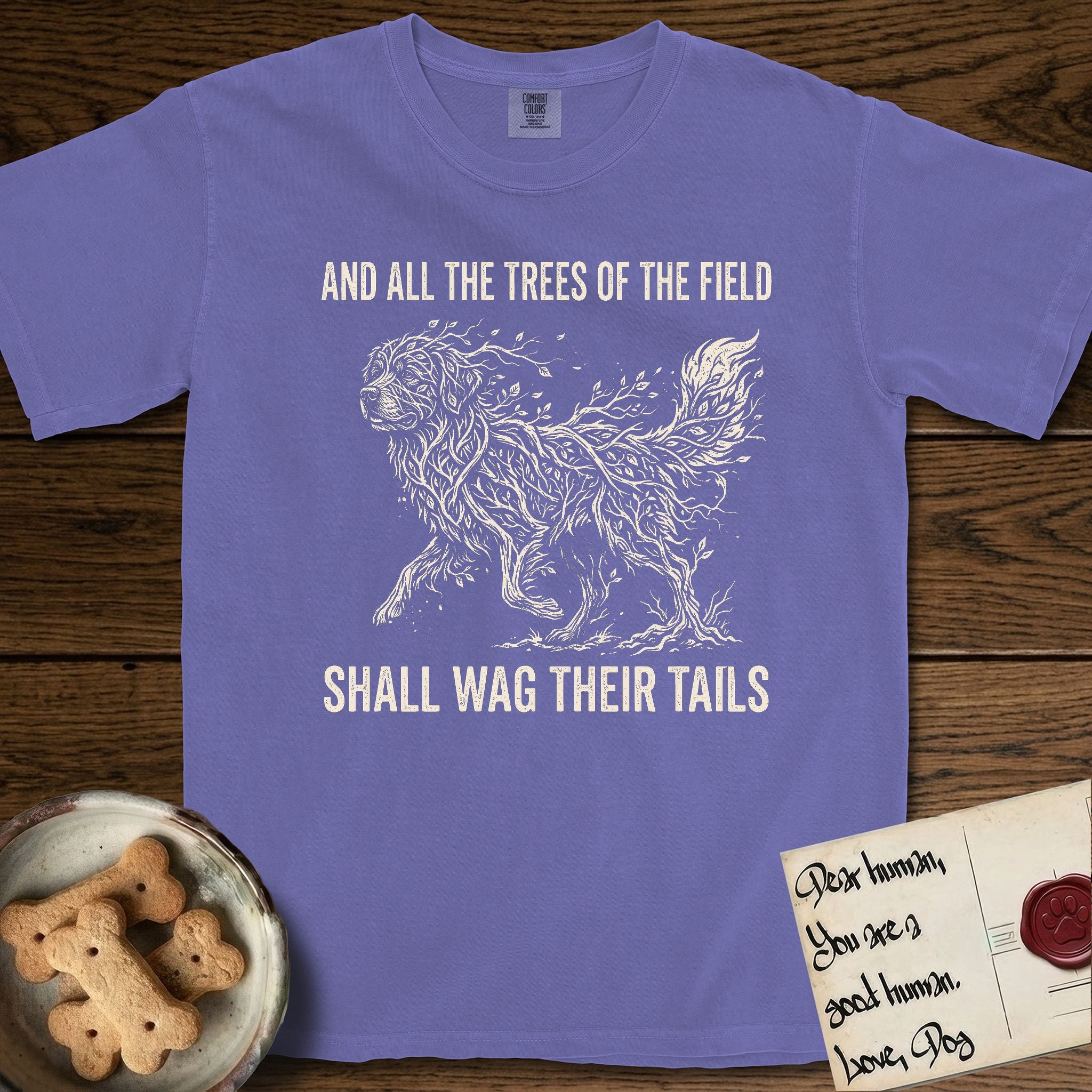 Trees of the Field Newfoundland T-Shirt flat lay in Violet, featuring a vintage woodcut illustration of a Newfoundland formed of linden branches in full leaf, mid-stride, with the words And All the Trees of the Field Shall Wag Their Tails.