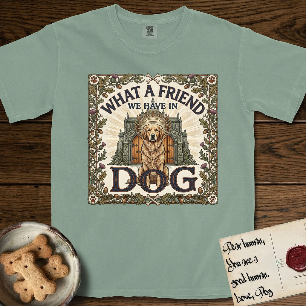 What a Friend We Have in Dog T-Shirt flat lay in Bay, featuring an Arts and Crafts tapestry illustration of a haloed Golden Retriever seated before a monastery, framed by an oak-leaf, acorn, and thistle border, with the word DOG below.