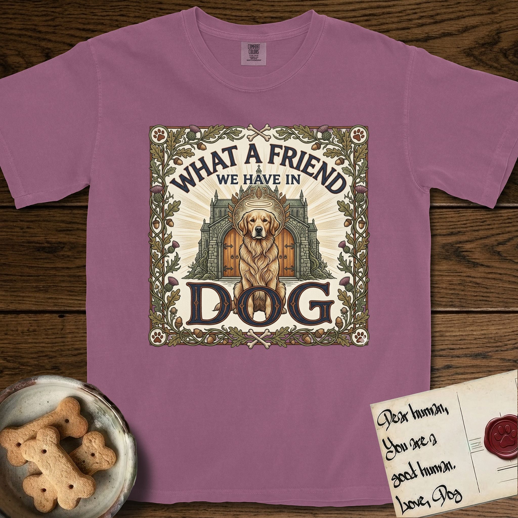 What a Friend We Have in Dog T-Shirt flat lay in Berry, featuring an Arts and Crafts tapestry illustration of a haloed Golden Retriever seated before a monastery, framed by an oak-leaf, acorn, and thistle border, with the word DOG below.