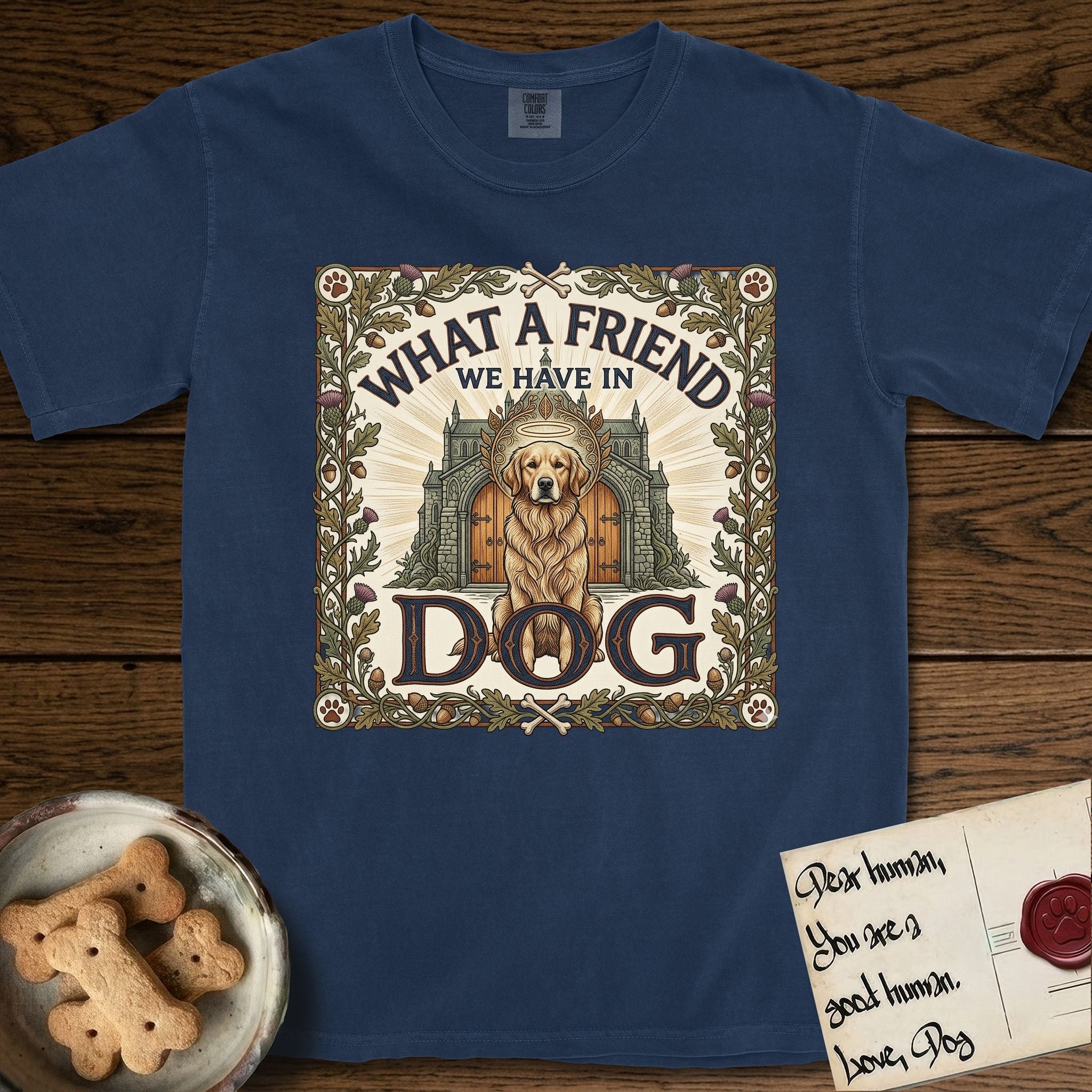 What a Friend We Have in Dog T-Shirt flat lay in True Navy, featuring an Arts and Crafts tapestry illustration of a haloed Golden Retriever seated before a monastery, framed by an oak-leaf, acorn, and thistle border, with the word DOG below.