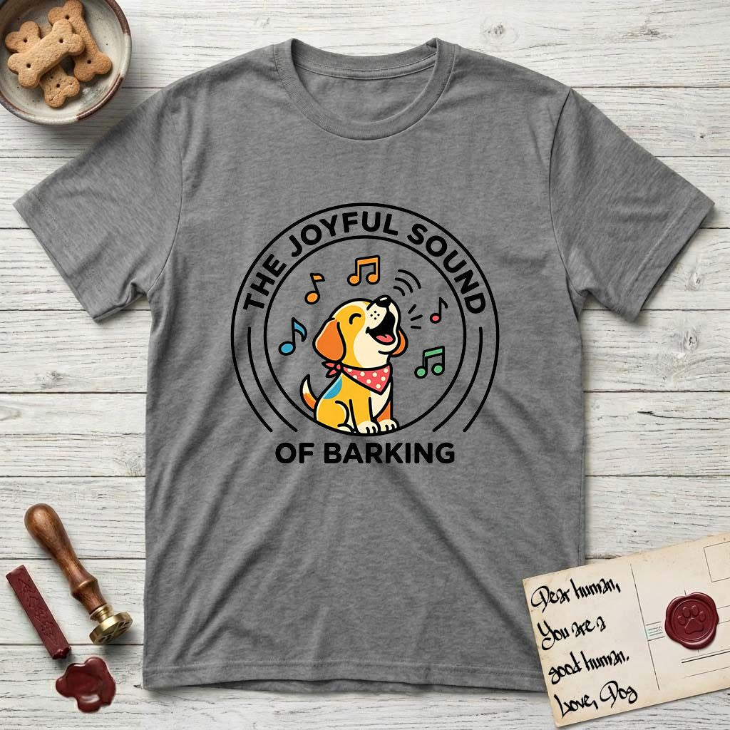 The Joyful Sound of Barking T-Shirt flat lay in Graphite Heather, featuring a flat vector cartoon emblem of a happy puppy with lifted ears surrounded by musical notes, ringed by the words The Joyful Sound of Barking.