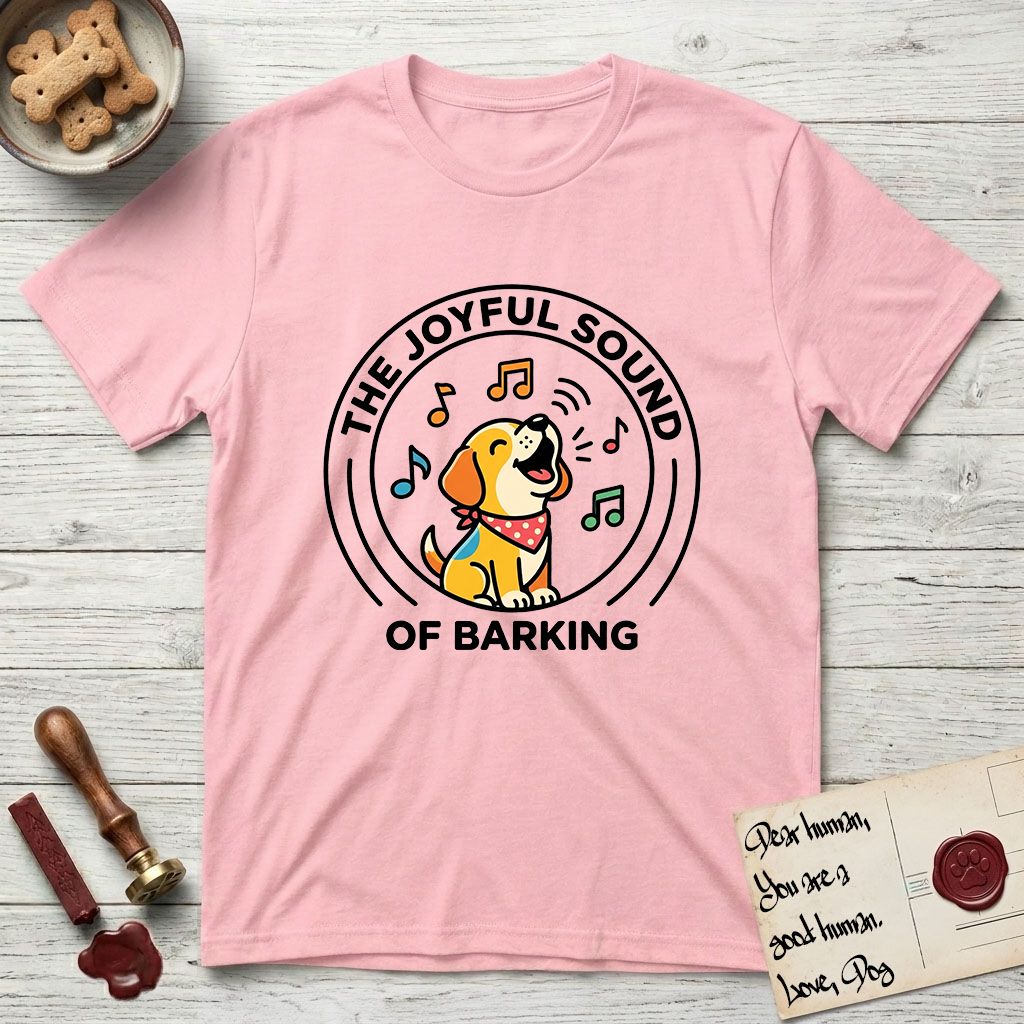 The Joyful Sound of Barking T-Shirt flat lay in Light Pink, featuring a flat vector cartoon emblem of a happy puppy with lifted ears surrounded by musical notes, ringed by the words The Joyful Sound of Barking.