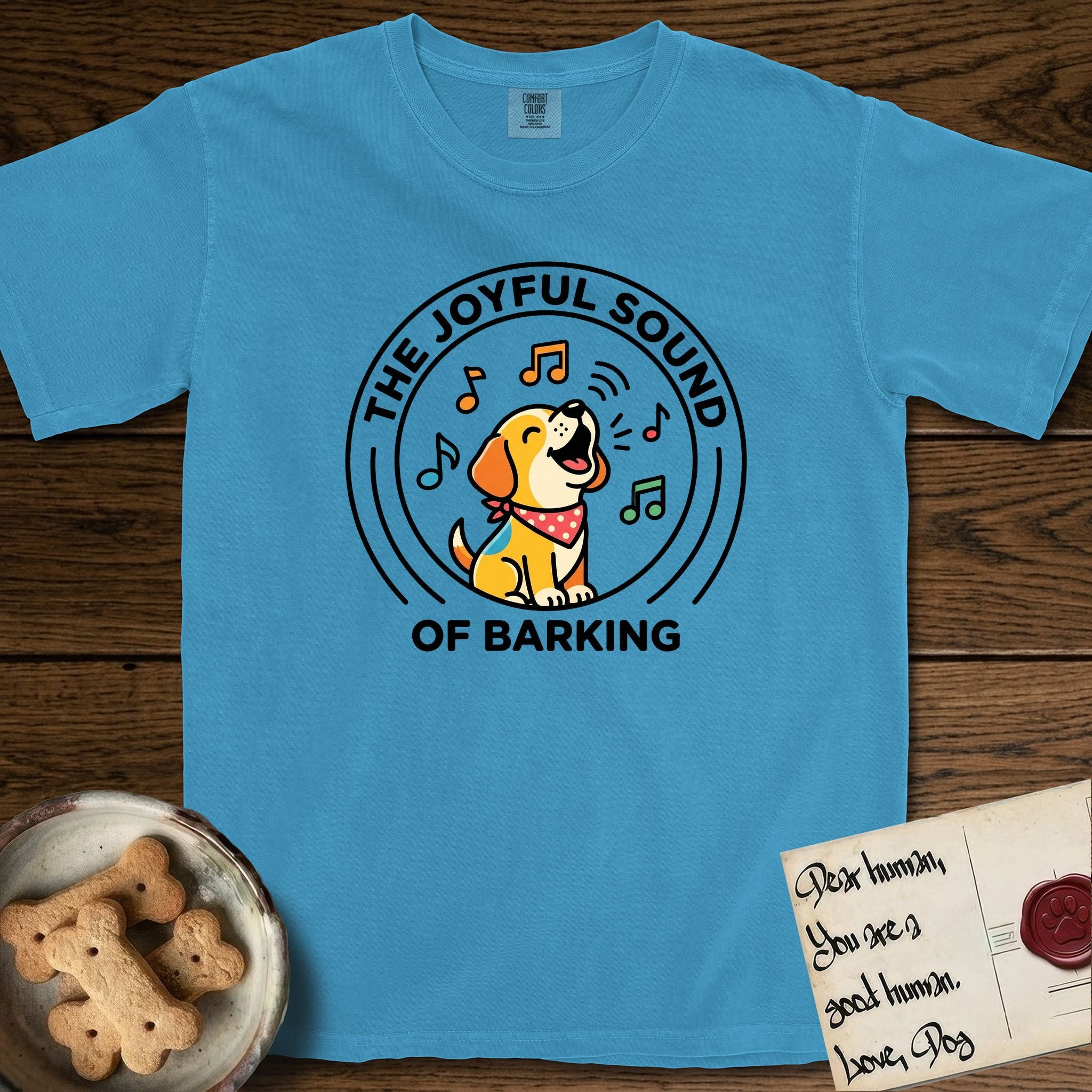 The Joyful Sound of Barking T-Shirt flat lay in Royal Caribe, featuring a flat vector cartoon emblem of a happy puppy with lifted ears surrounded by musical notes, ringed by the words The Joyful Sound of Barking.