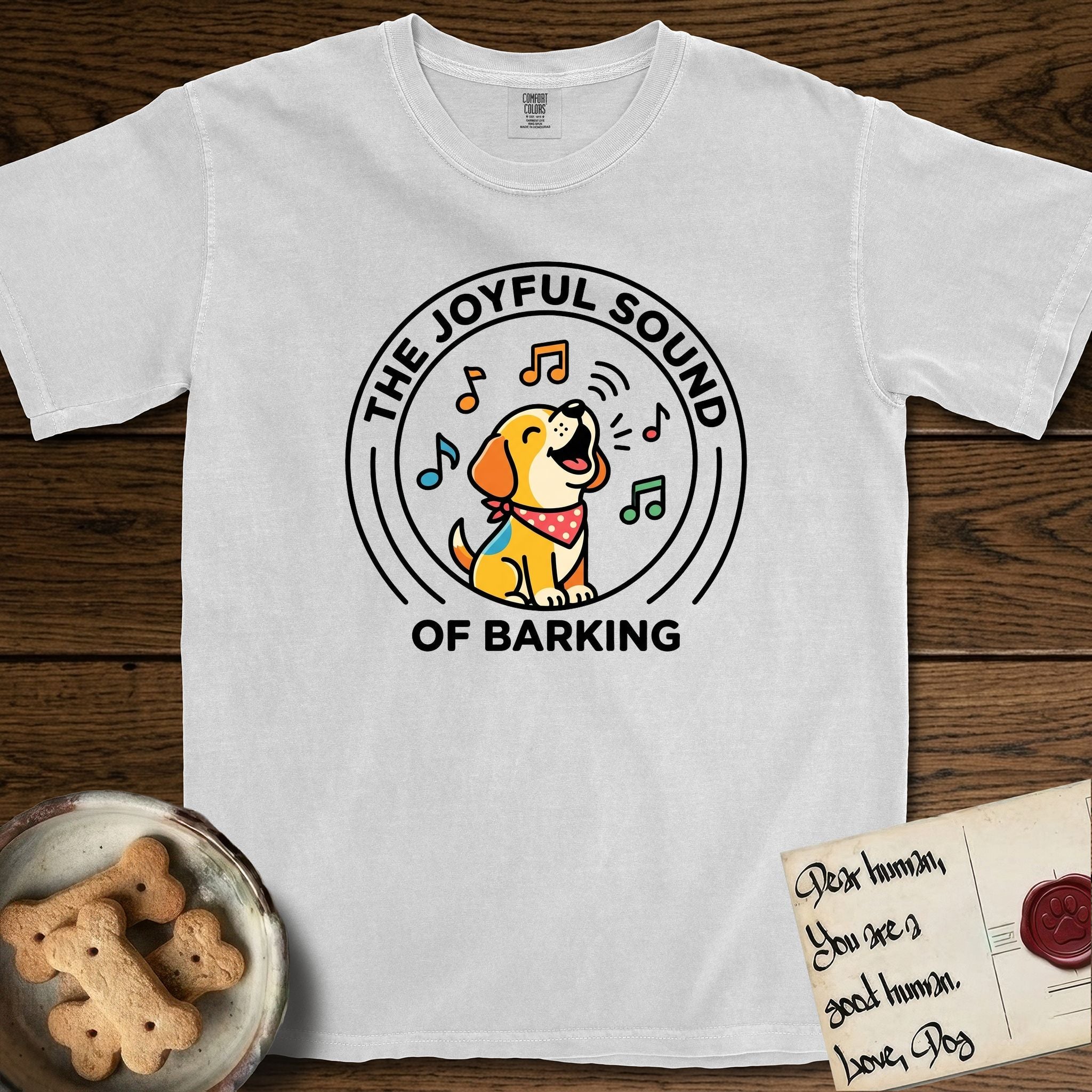 The Joyful Sound of Barking T-Shirt flat lay in White, featuring a flat vector cartoon emblem of a happy puppy with lifted ears surrounded by musical notes, ringed by the words The Joyful Sound of Barking.
