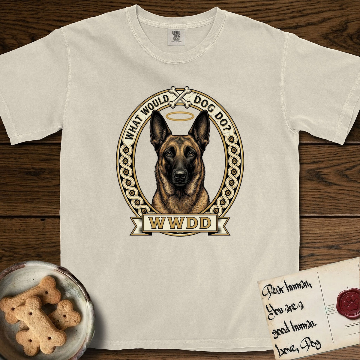 What Would Dog Do Belgian Malinois T-Shirt flat lay in Ivory, featuring a vintage gold portrait medallion of a haloed Belgian Malinois in an ornamental rosette-scroll border with the question What Would Dog Do.