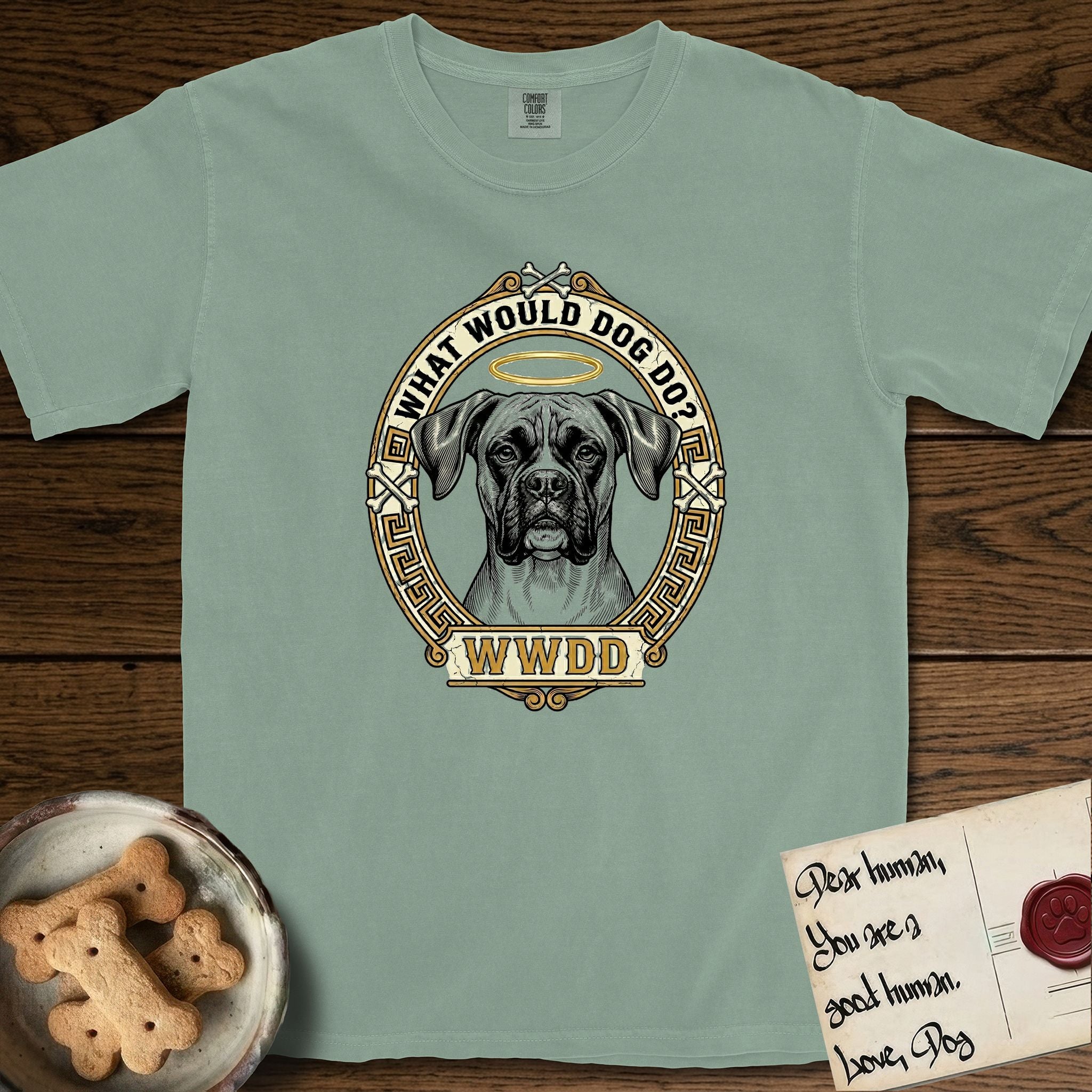 What Would Dog Do Boxer T-Shirt flat lay in Bay, featuring a Greek-key bordered gold portrait medallion of a haloed Boxer with natural uncropped ears and the question What Would Dog Do.