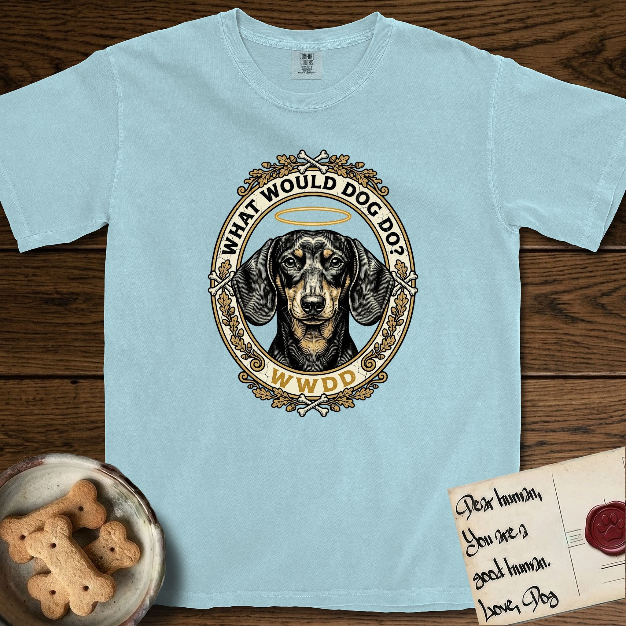 What Would Dog Do Dachshund T-Shirt flat lay in Chambray, featuring an oak-leaf and acorn framed gold portrait medallion of a haloed Dachshund with the question What Would Dog Do.