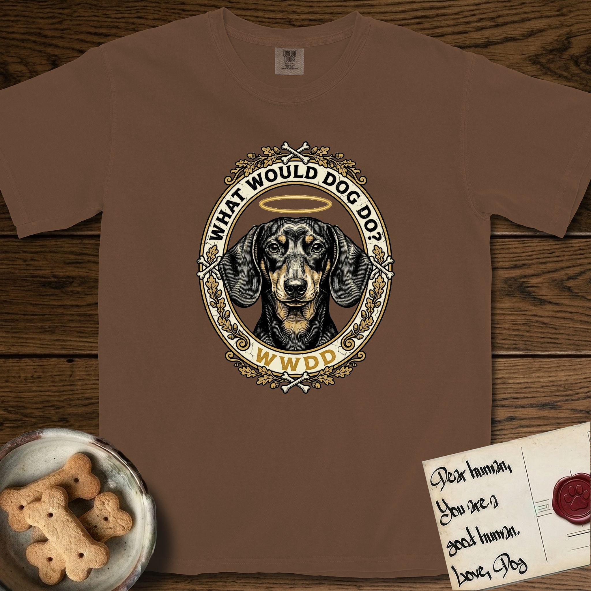 What Would Dog Do Dachshund T-Shirt flat lay in Espresso, featuring an oak-leaf and acorn framed gold portrait medallion of a haloed Dachshund with the question What Would Dog Do.