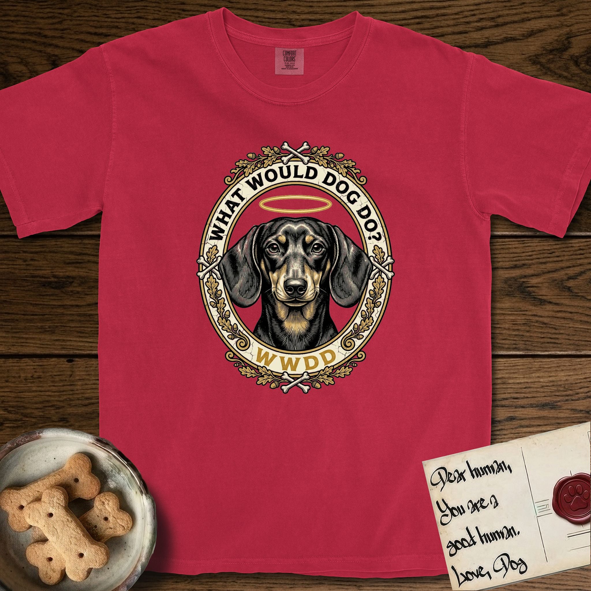 What Would Dog Do Dachshund T-Shirt flat lay in Red, featuring an oak-leaf and acorn framed gold portrait medallion of a haloed Dachshund with the question What Would Dog Do.