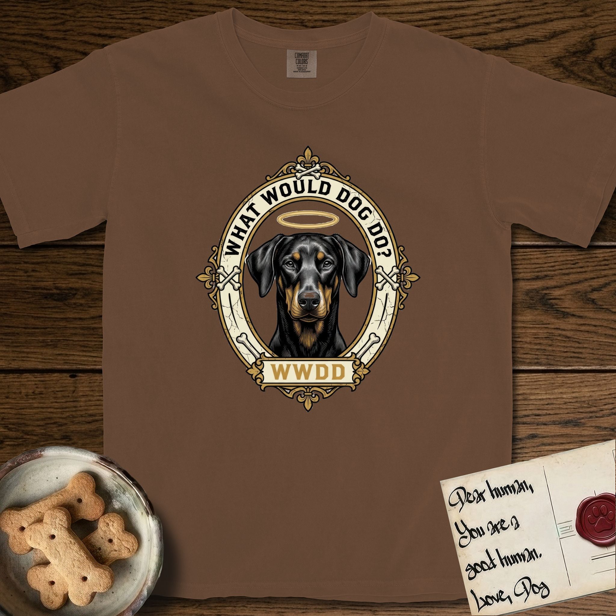 What Would Dog Do Doberman T-Shirt flat lay in Espresso, featuring a fleur-de-lis framed gold portrait medallion of a haloed Doberman with natural uncropped ears and the question What Would Dog Do.