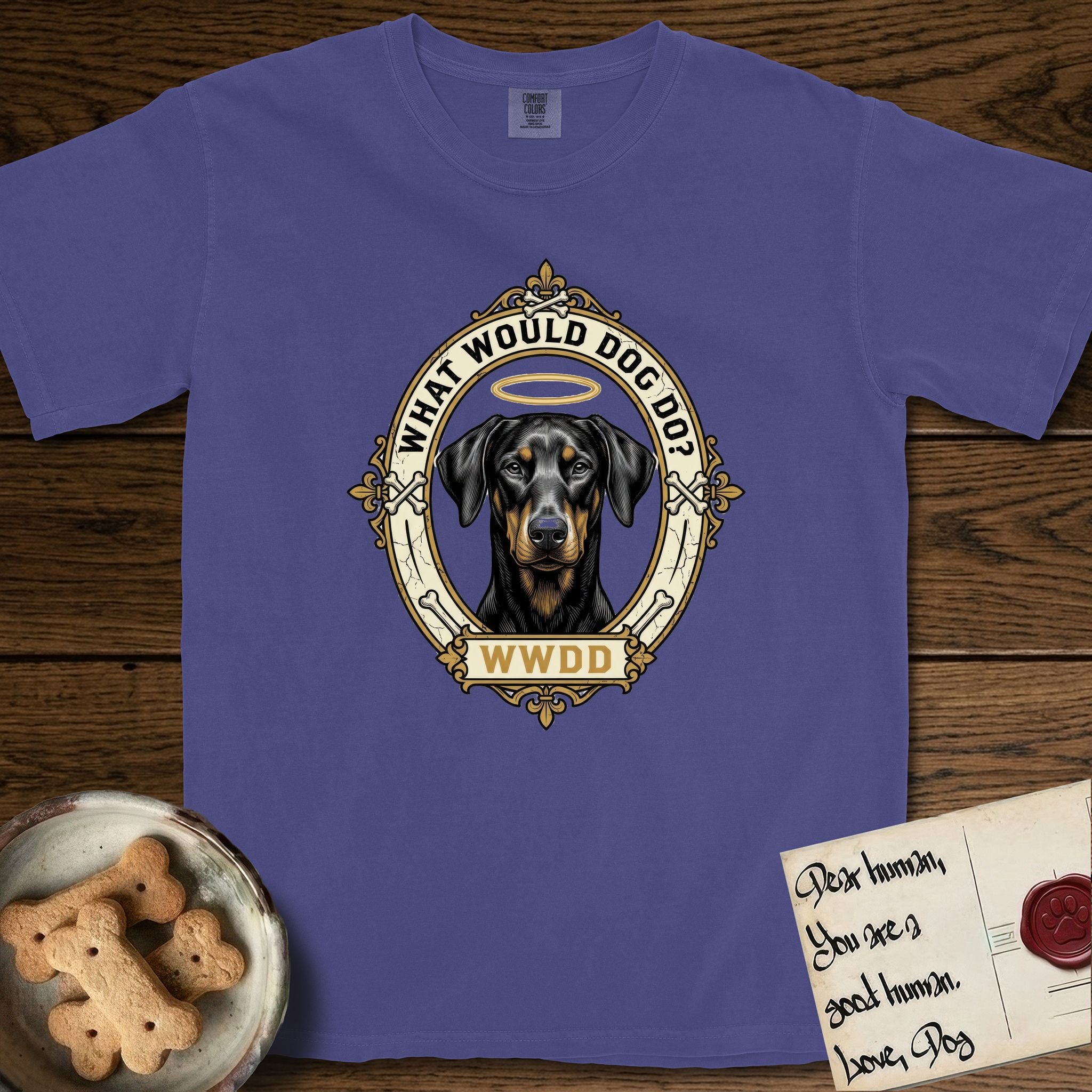 What Would Dog Do Doberman T-Shirt flat lay in Grape, featuring a fleur-de-lis framed gold portrait medallion of a haloed Doberman with natural uncropped ears and the question What Would Dog Do.