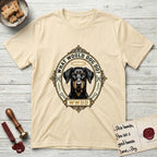 What Would Dog Do Doberman T-Shirt flat lay in Natural, featuring a fleur-de-lis framed gold portrait medallion of a haloed Doberman with natural uncropped ears and the question What Would Dog Do.
