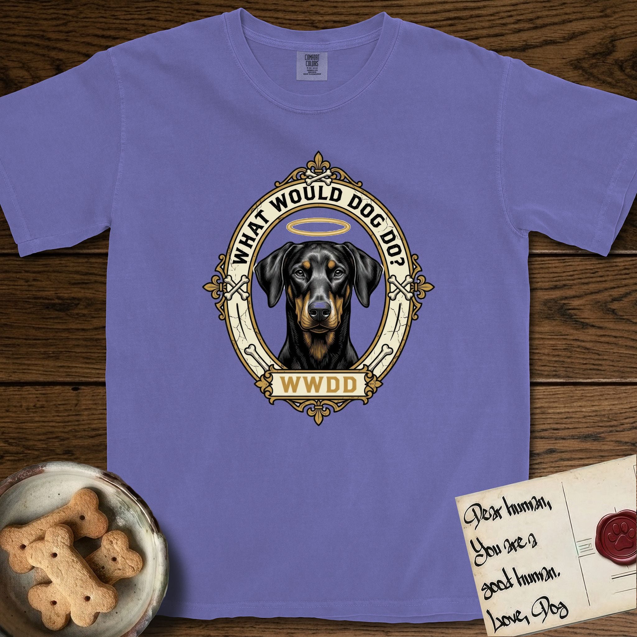 What Would Dog Do Doberman T-Shirt flat lay in Violet, featuring a fleur-de-lis framed gold portrait medallion of a haloed Doberman with natural uncropped ears and the question What Would Dog Do.