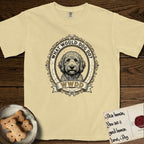 What Would Dog Do Goldendoodle T-Shirt flat lay in Butter, featuring an ornate scrollwork gold portrait medallion of a haloed Goldendoodle with the question What Would Dog Do.