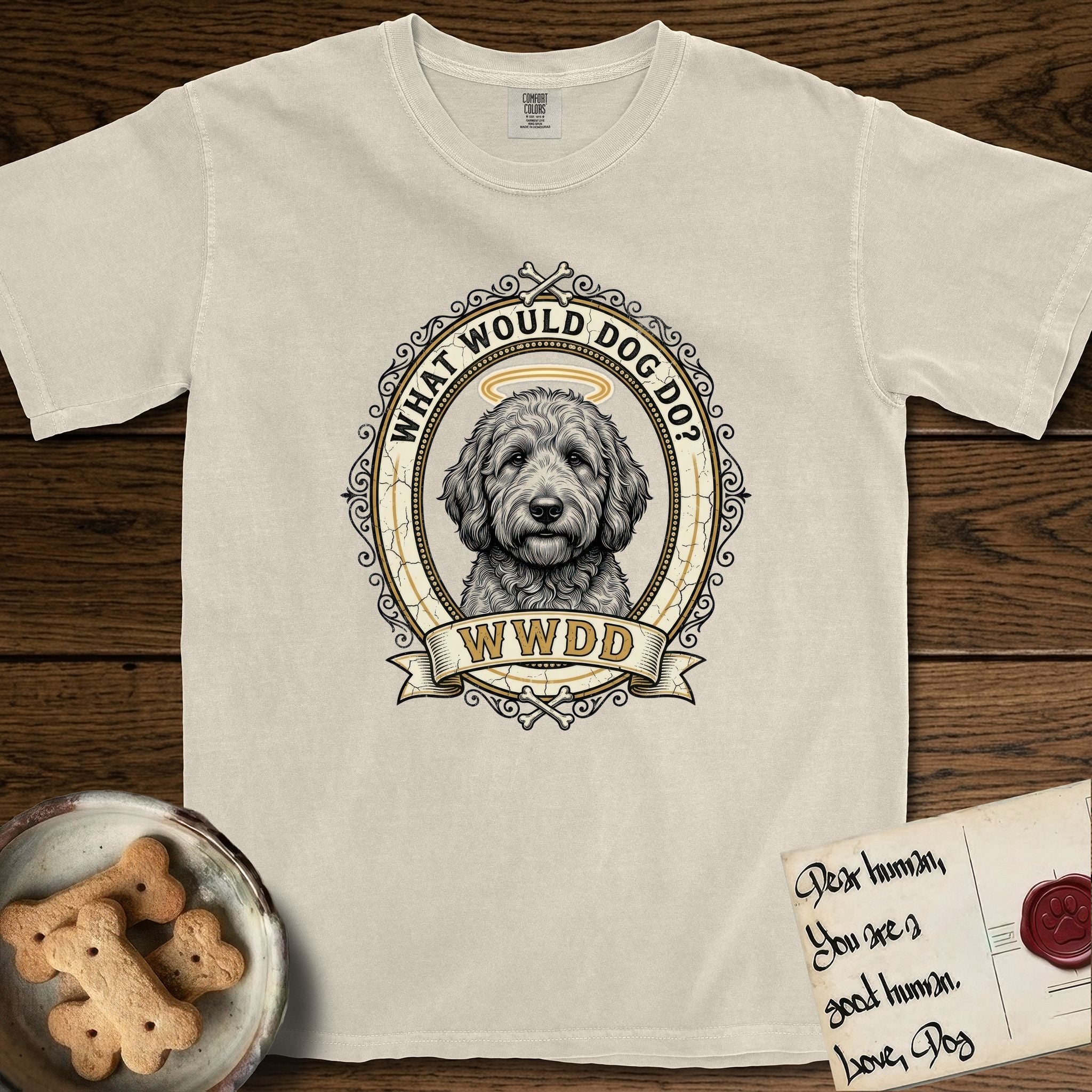 What Would Dog Do Goldendoodle T-Shirt flat lay in Ivory, featuring an ornate scrollwork gold portrait medallion of a haloed Goldendoodle with the question What Would Dog Do.