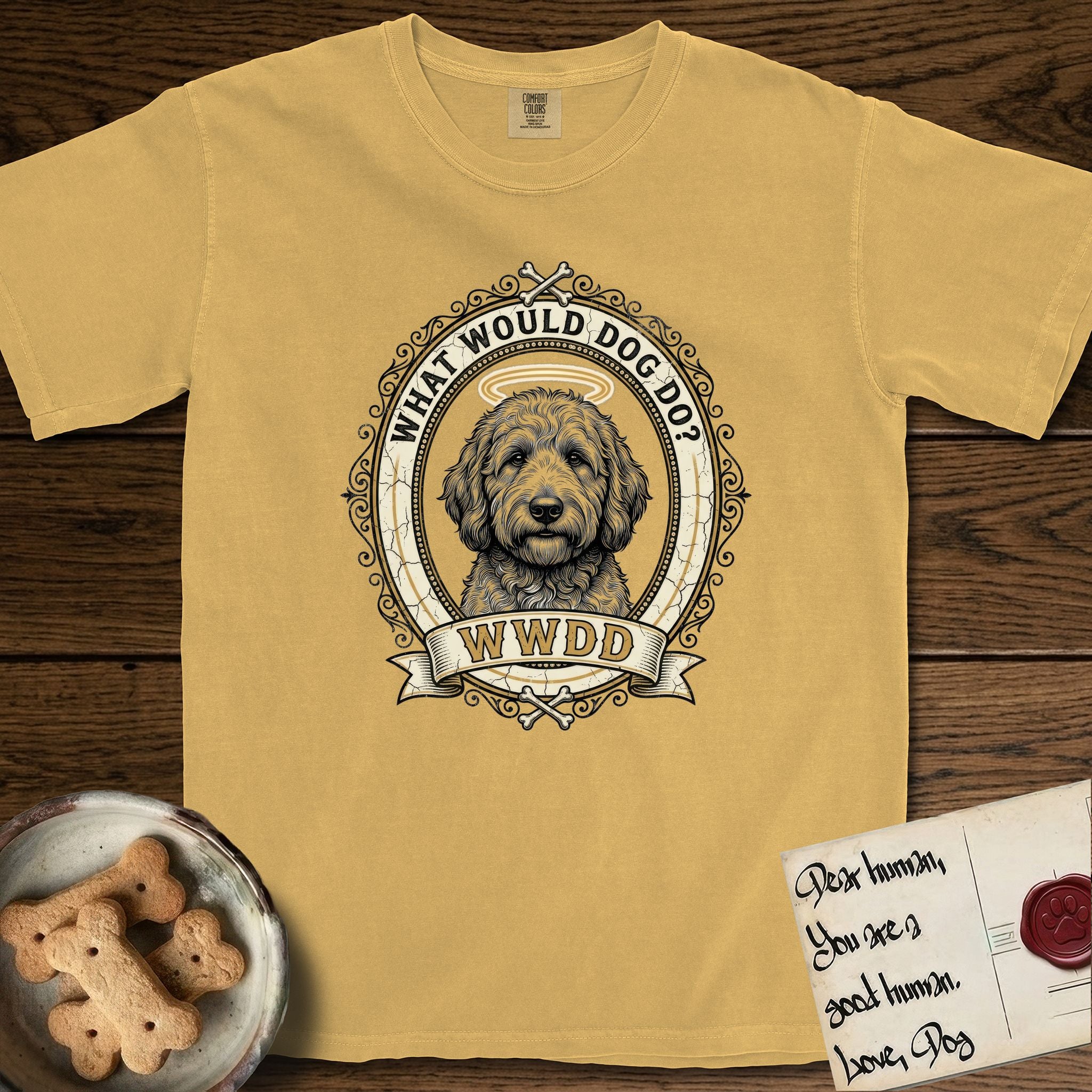 What Would Dog Do Goldendoodle T-Shirt flat lay in Mustard, featuring an ornate scrollwork gold portrait medallion of a haloed Goldendoodle with the question What Would Dog Do.