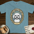 What Would Dog Do Maltese T-Shirt flat lay in Ice Blue, featuring a vintage gold portrait medallion of a haloed white Maltese in a Celtic knotwork and rope border with the question What Would Dog Do.
