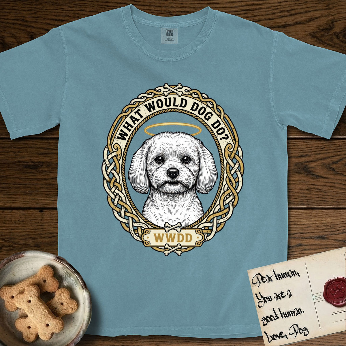 What Would Dog Do Maltese T-Shirt flat lay in Ice Blue, featuring a vintage gold portrait medallion of a haloed white Maltese in a Celtic knotwork and rope border with the question What Would Dog Do.