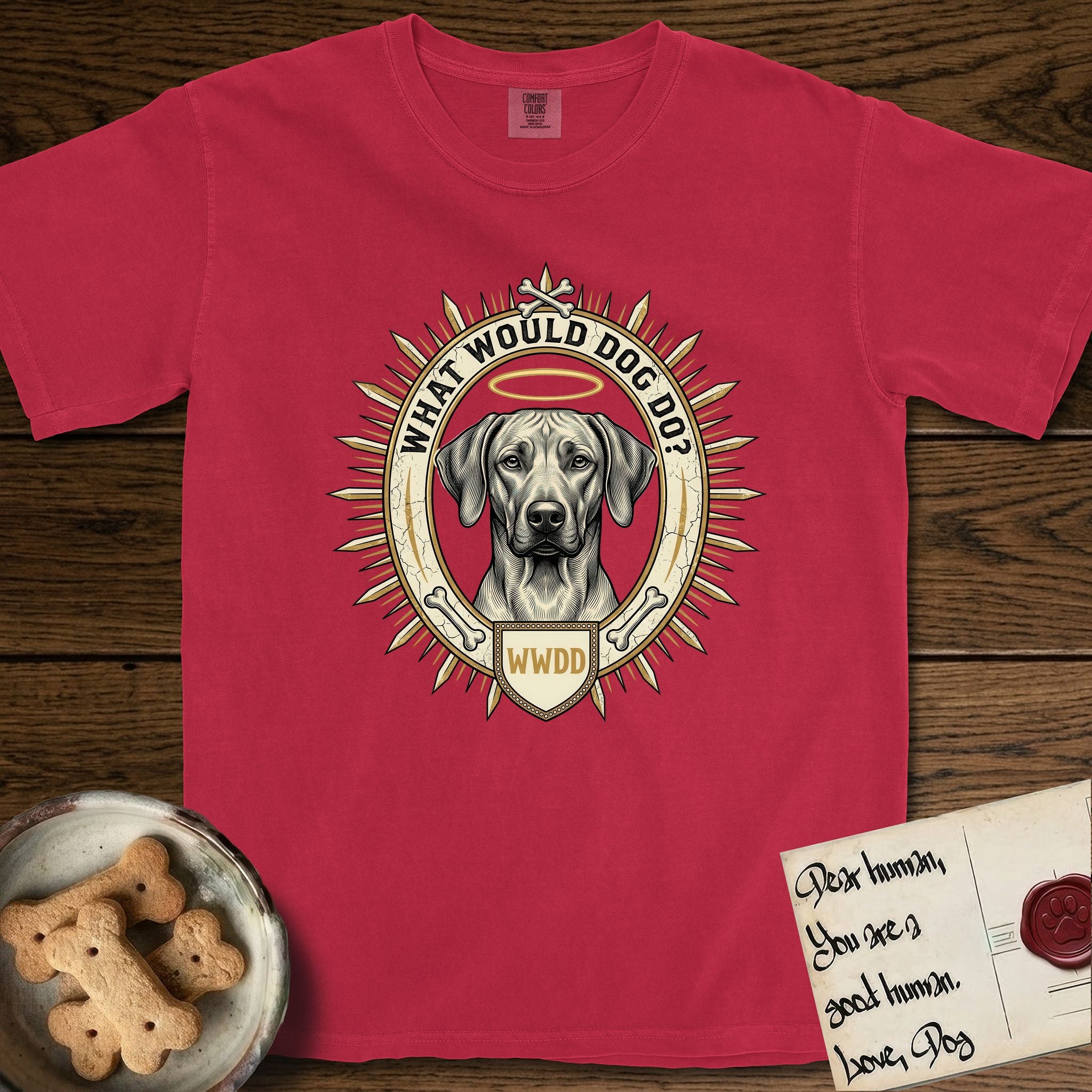 What Would Dog Do Rhodesian Ridgeback T-Shirt flat lay in Red, featuring a vintage gold portrait medallion of a haloed Rhodesian Ridgeback ringed by radiating sunburst spikes with the question What Would Dog Do.