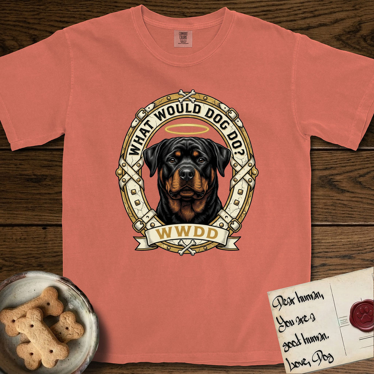 What Would Dog Do Rottweiler T-Shirt flat lay in Terracotta, featuring a vintage gold portrait medallion of a haloed Rottweiler framed by studded leather collar straps and buckles with the question What Would Dog Do.