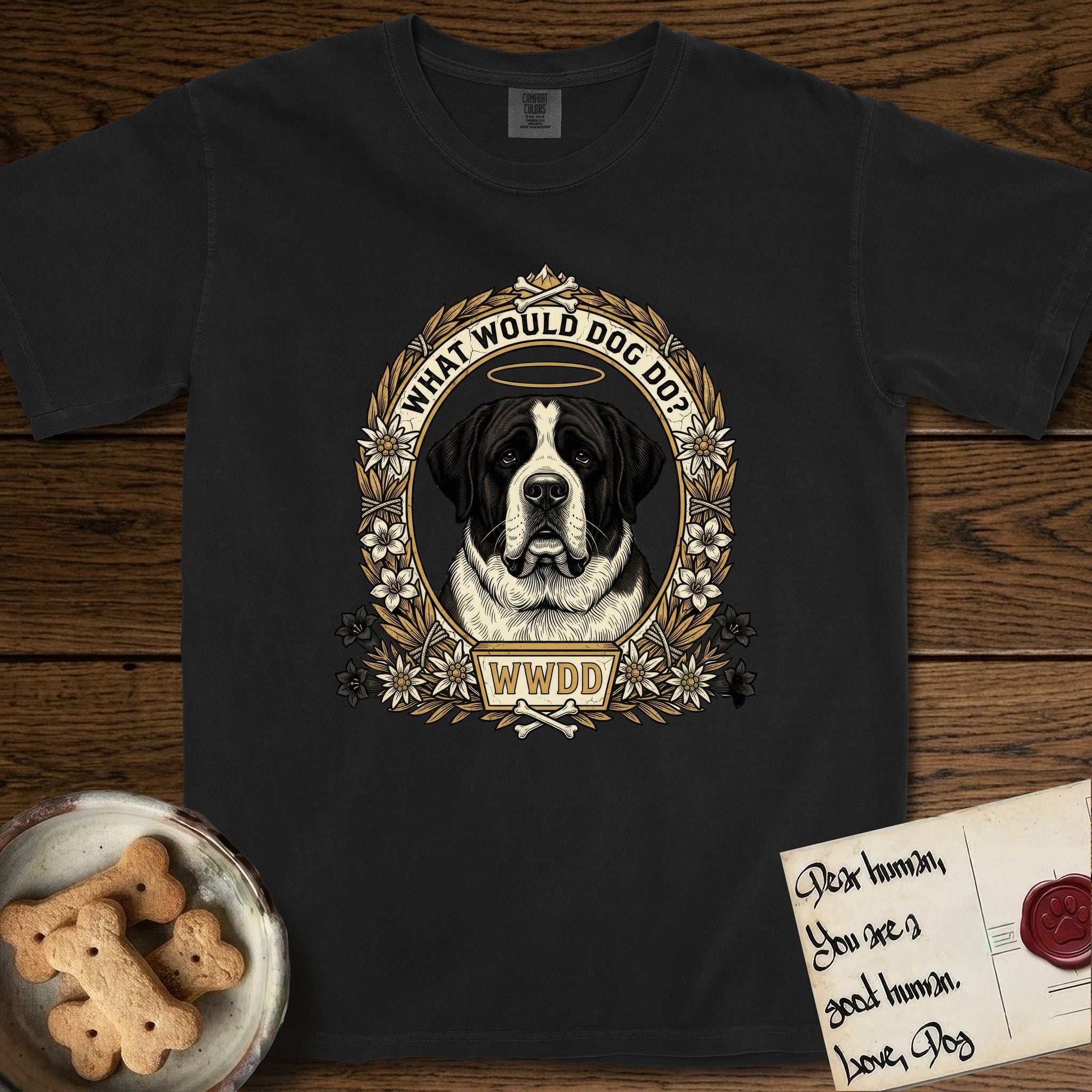 What Would Dog Do Saint Bernard T-Shirt flat lay in Black, featuring a vintage gold portrait medallion of a haloed Saint Bernard in an alpine laurel wreath with edelweiss blossoms and the question What Would Dog Do.