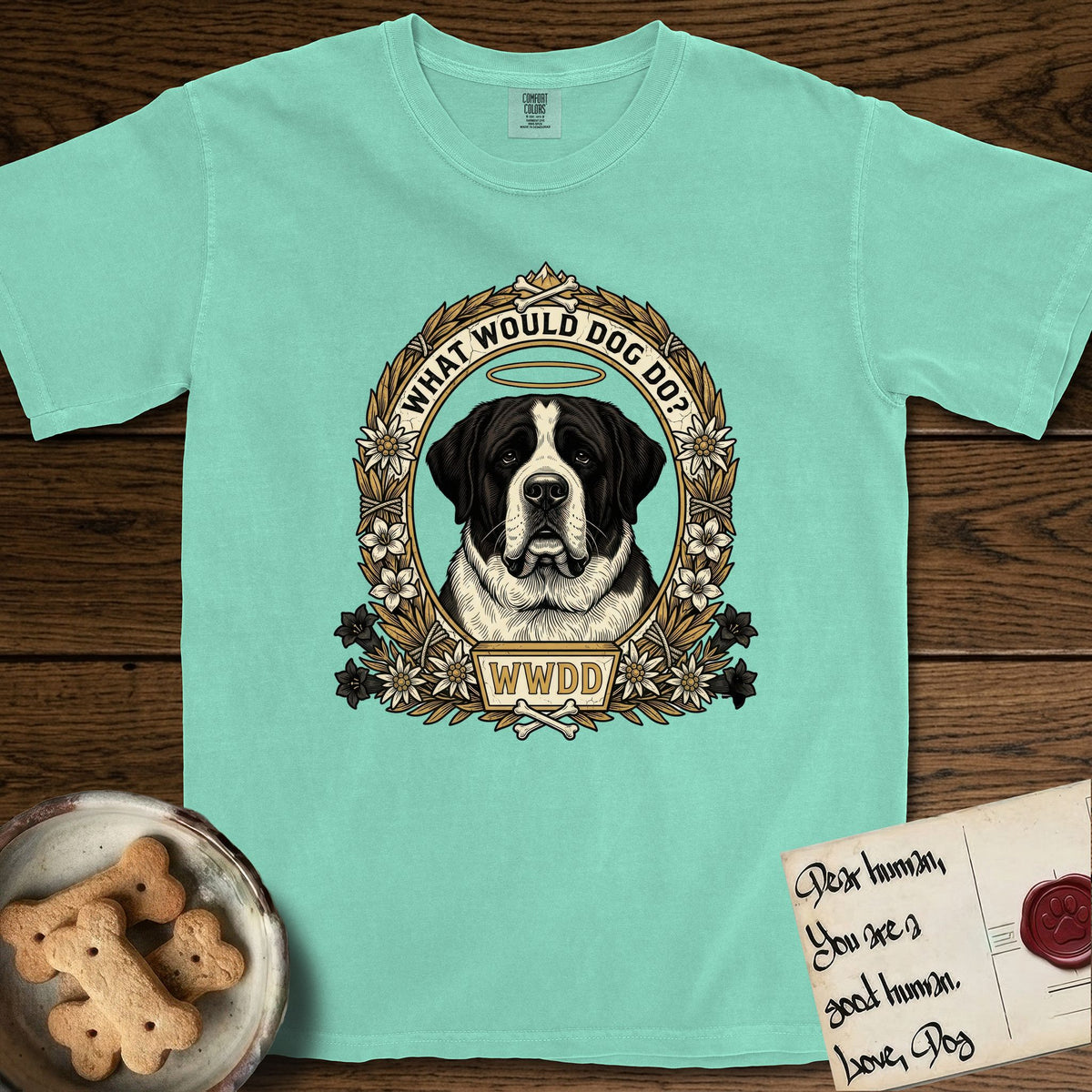 What Would Dog Do Saint Bernard T-Shirt flat lay in Island Reef, featuring a vintage gold portrait medallion of a haloed Saint Bernard in an alpine laurel wreath with edelweiss blossoms and the question What Would Dog Do.
