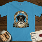 What Would Dog Do Saint Bernard T-Shirt flat lay in Royal Caribe, featuring a vintage gold portrait medallion of a haloed Saint Bernard in an alpine laurel wreath with edelweiss blossoms and the question What Would Dog Do.