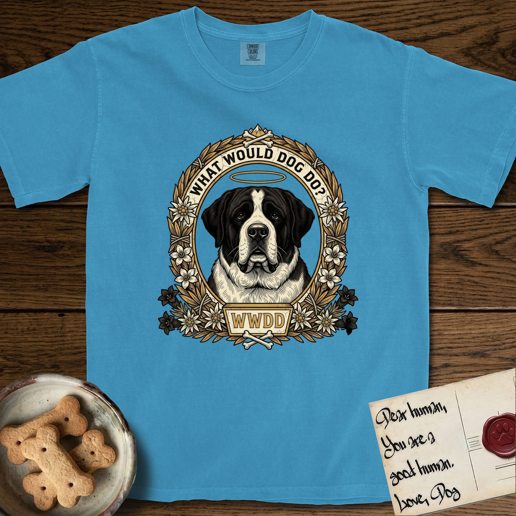 What Would Dog Do Saint Bernard T-Shirt flat lay in Royal Caribe, featuring a vintage gold portrait medallion of a haloed Saint Bernard in an alpine laurel wreath with edelweiss blossoms and the question What Would Dog Do.
