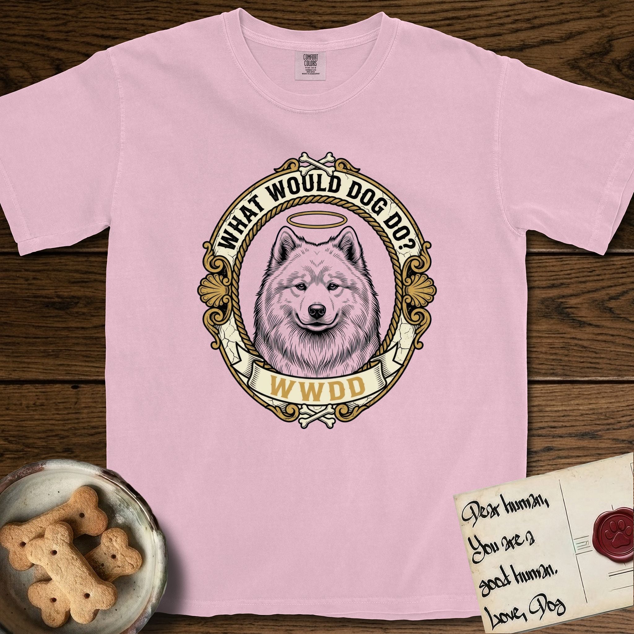 What Would Dog Do Samoyed T-Shirt flat lay in Blossom, featuring a rope-twist framed gold portrait medallion of a haloed Samoyed with the question What Would Dog Do.