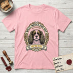 What Would Dog Do Spaniel T-Shirt flat lay in Light Pink, featuring a rose-bordered gold portrait medallion of a haloed Cavalier King Charles Spaniel with the question What Would Dog Do.