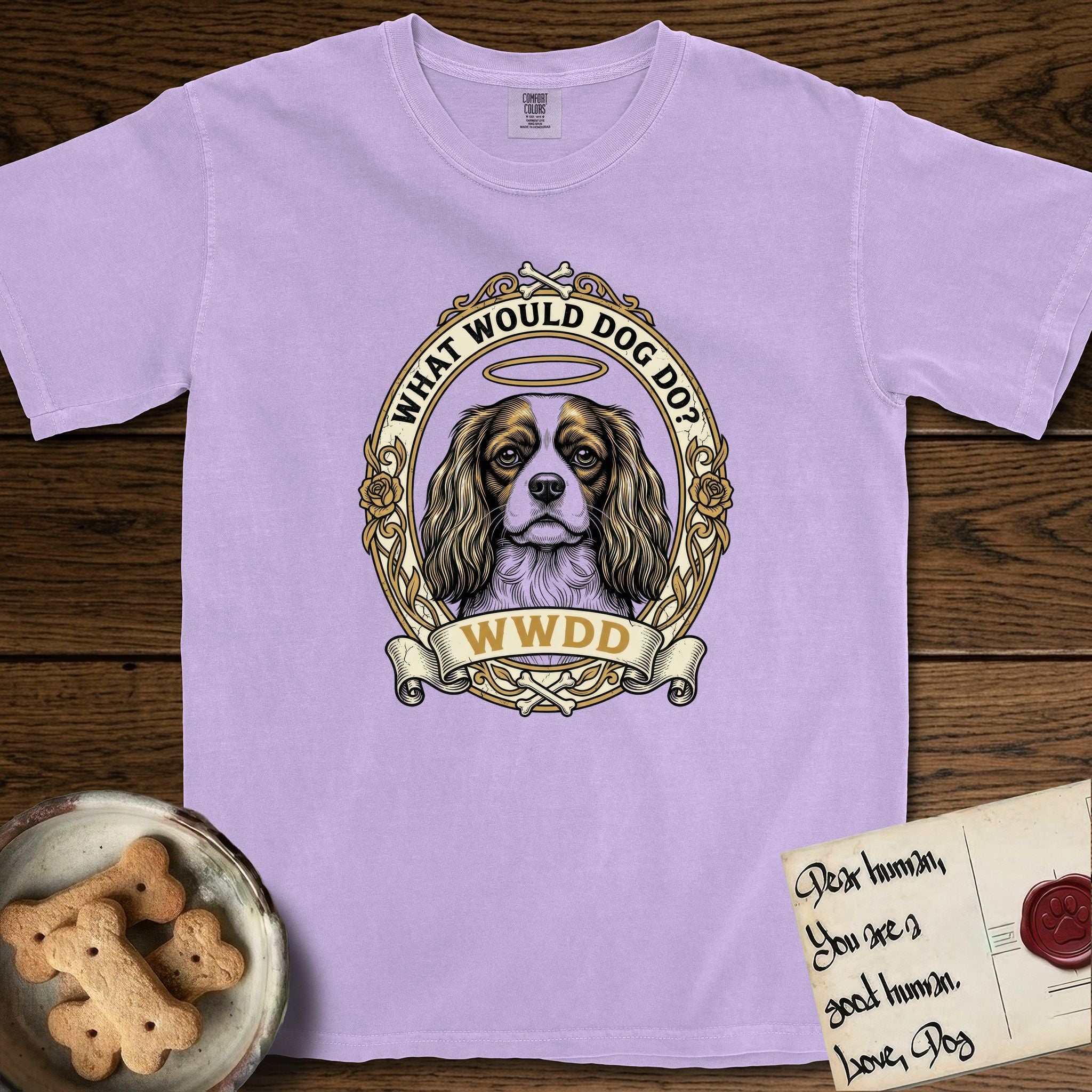 What Would Dog Do Cavalier T-Shirt flat lay in Orchid, featuring a rose-bordered gold portrait medallion of a haloed Cavalier King Charles Spaniel with the question What Would Dog Do.