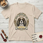 What Would Dog Do Spaniel T-Shirt flat lay in Sand, featuring a rose-bordered gold portrait medallion of a haloed Cavalier King Charles Spaniel with the question What Would Dog Do.