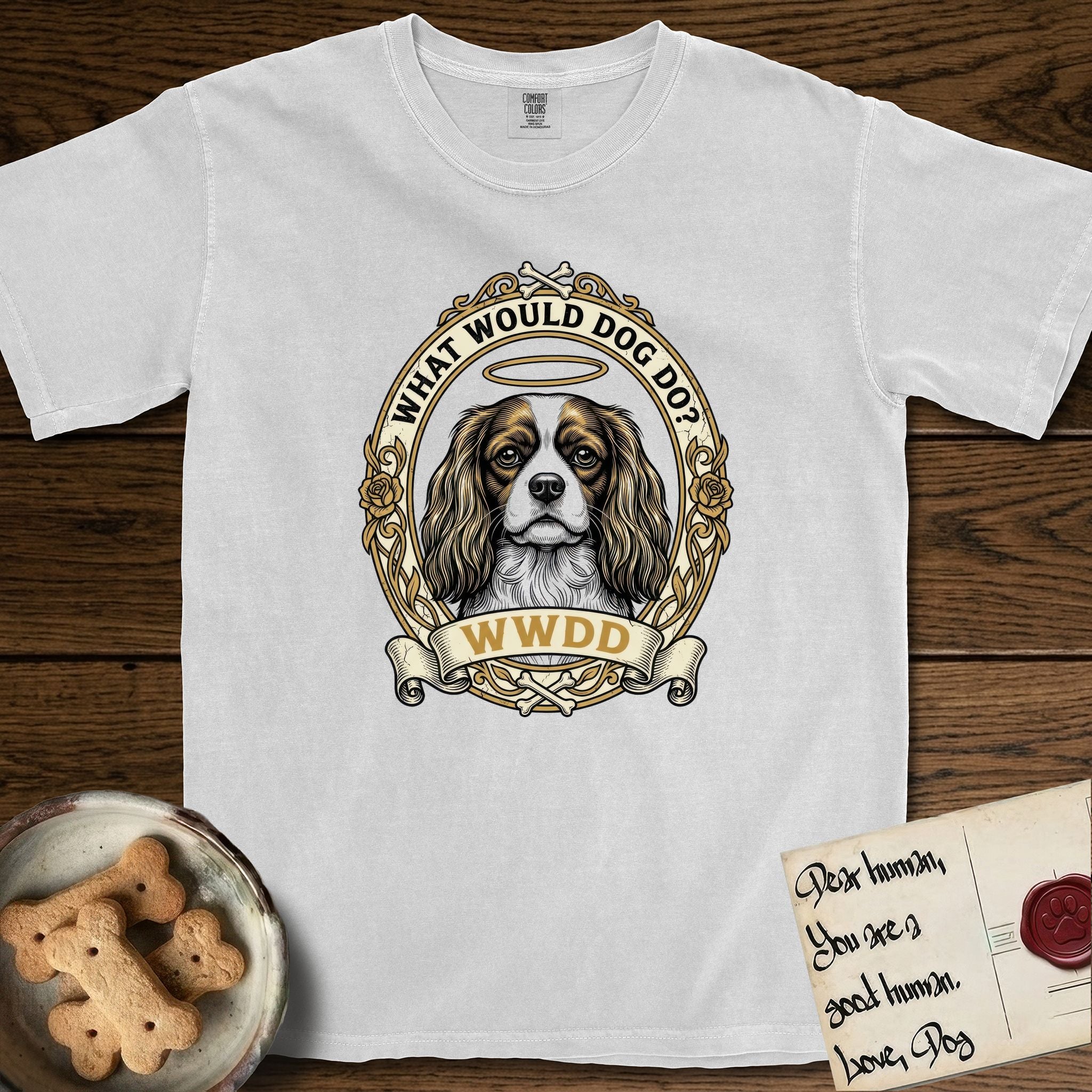What Would Dog Do Cavalier T-Shirt flat lay in White, featuring a rose-bordered gold portrait medallion of a haloed Cavalier King Charles Spaniel with the question What Would Dog Do.